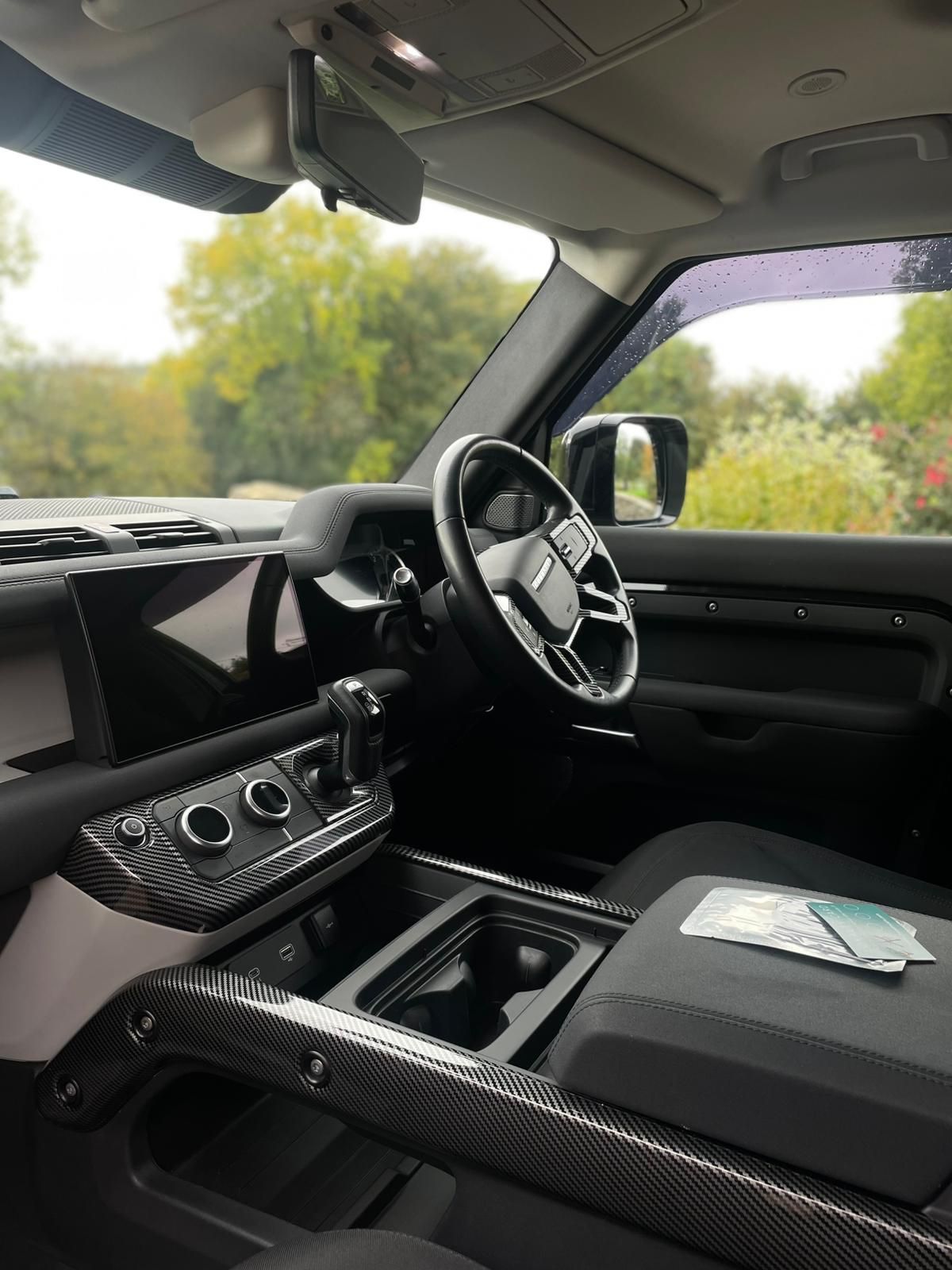 Interior of a Land Rover Defender, showing dashboard, steering wheel, seats, and center console with cup holders.