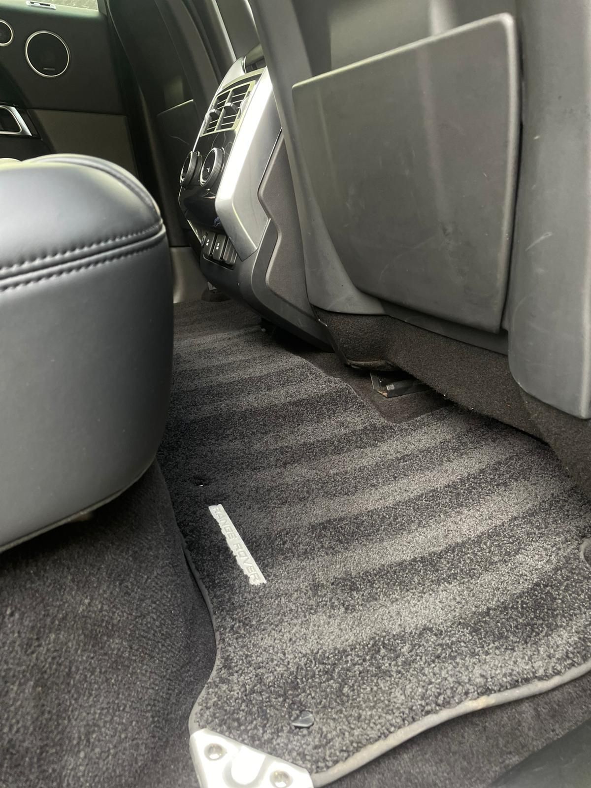 Car interior: Black carpet and seat, floor mat, and back seat storage compartment.