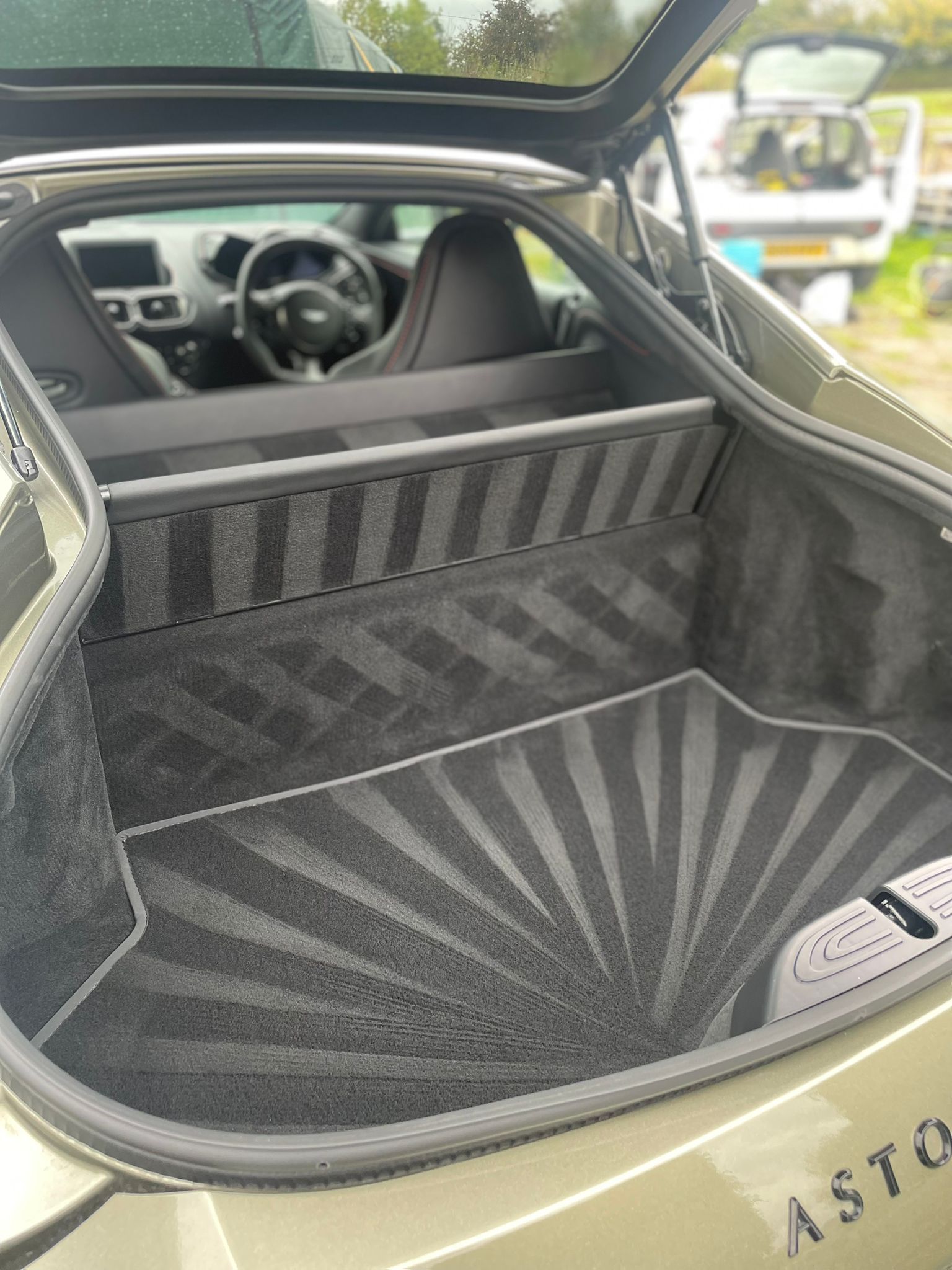 Open car trunk with patterned gray carpet interior; steering wheel visible.