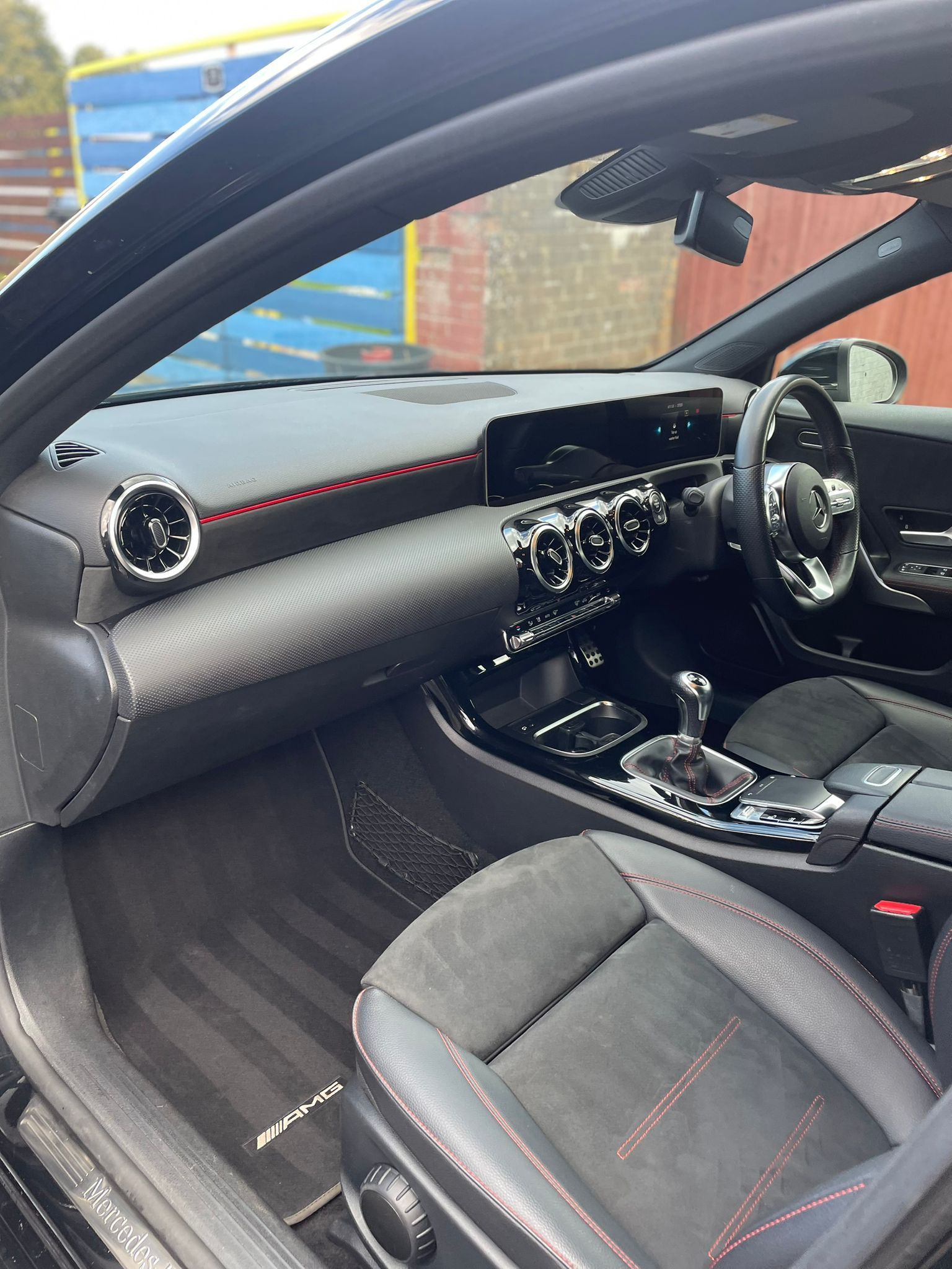 Black Mercedes-Benz interior with dashboard, seats, and steering wheel visible; red accents.