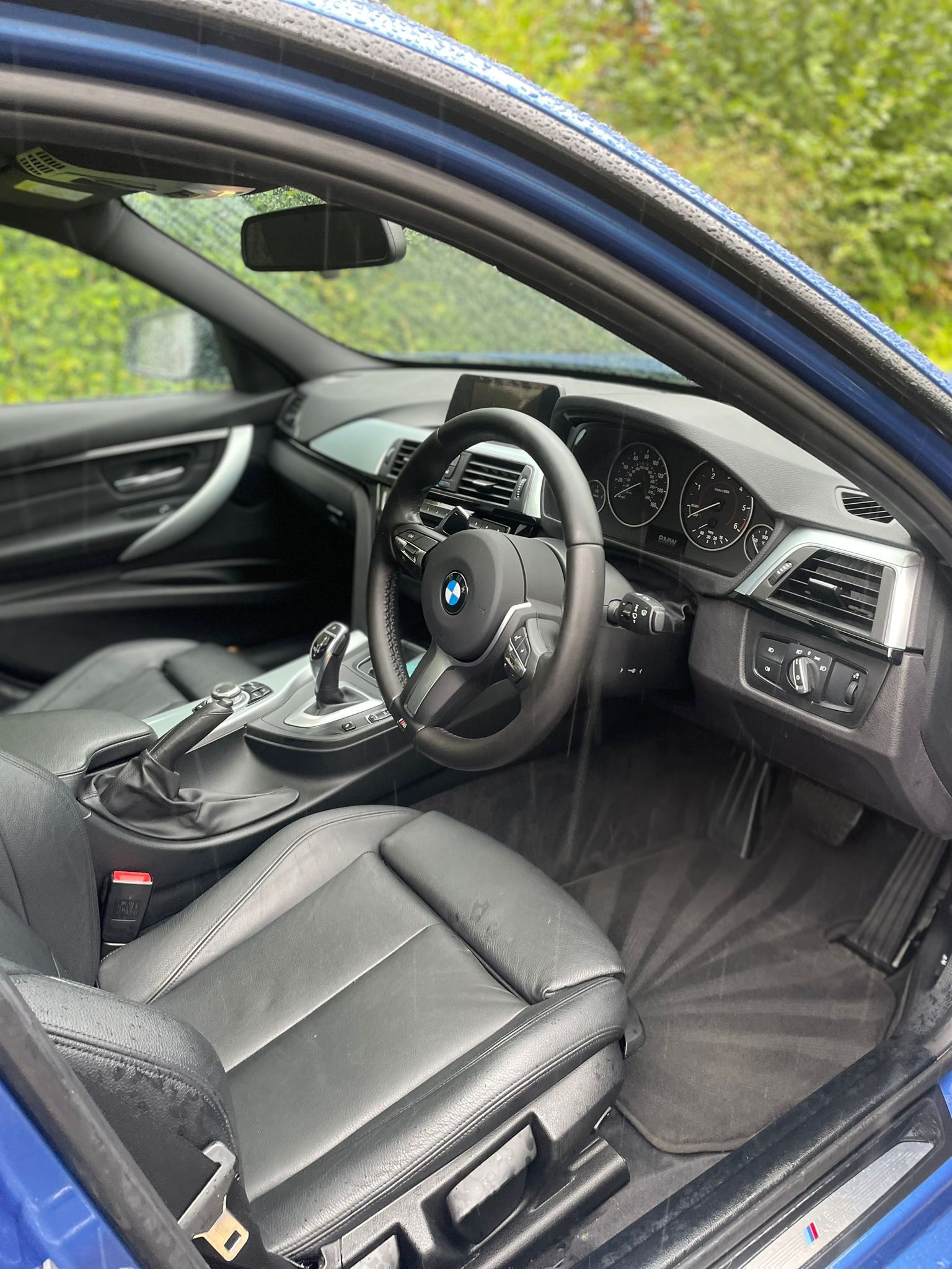 Interior of a blue BMW car with black leather seats, dashboard, and steering wheel.