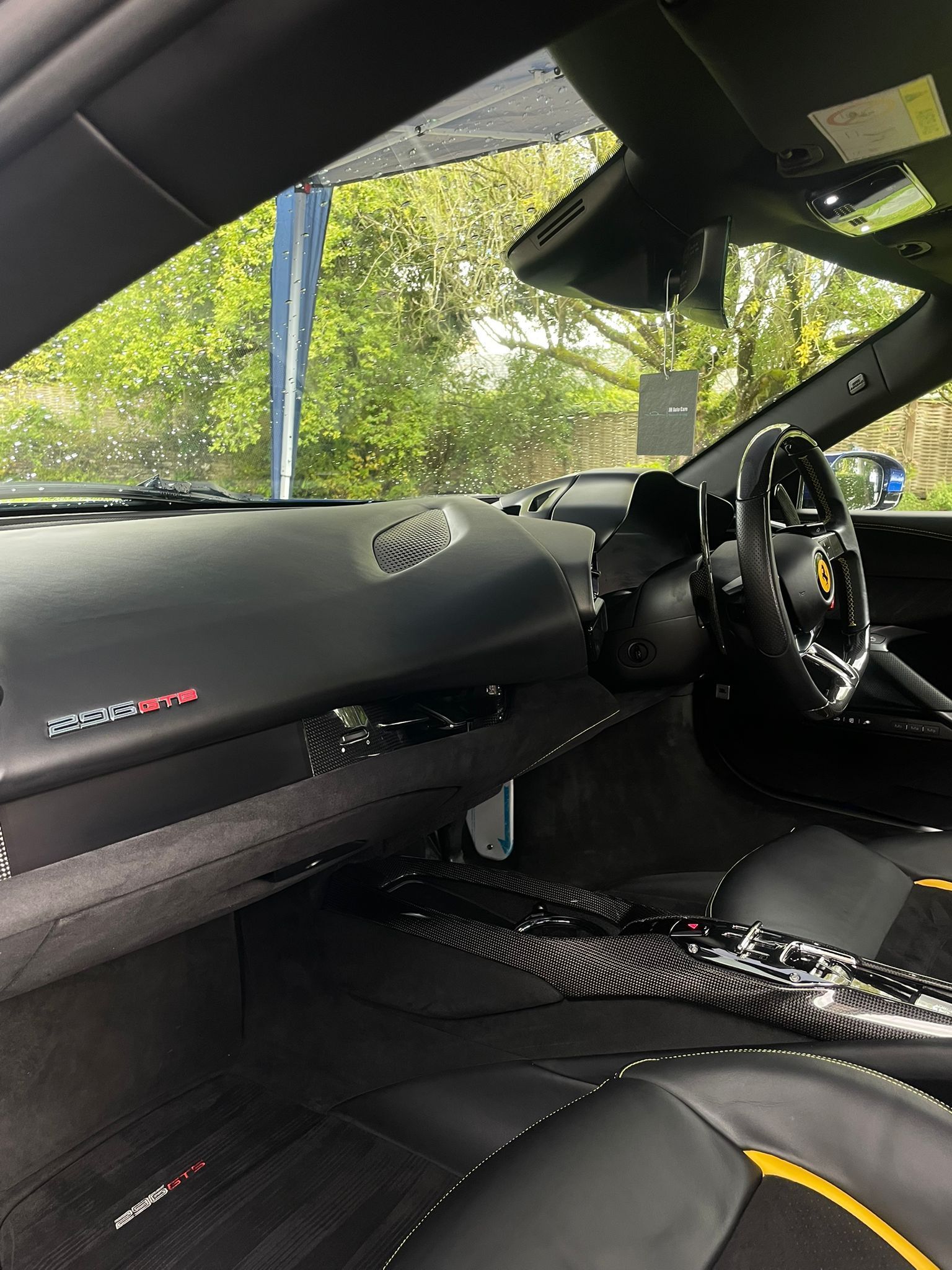 Interior of a black sports car with carbon fiber accents, yellow stitching, and a red emblem on the dashboard.