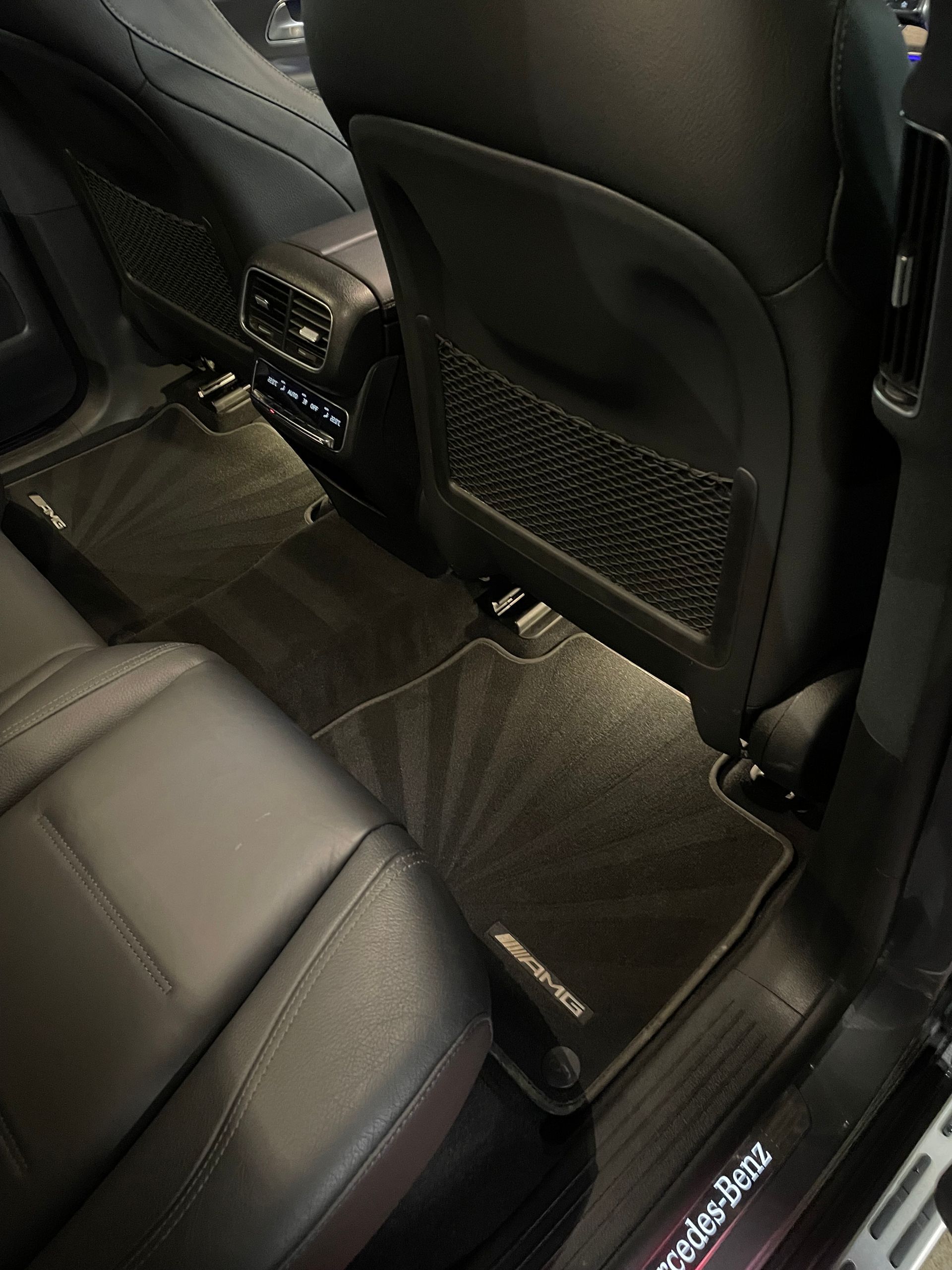 Black leather car interior with detailed floor mats; back seats visible. Mercedes-Benz logo.