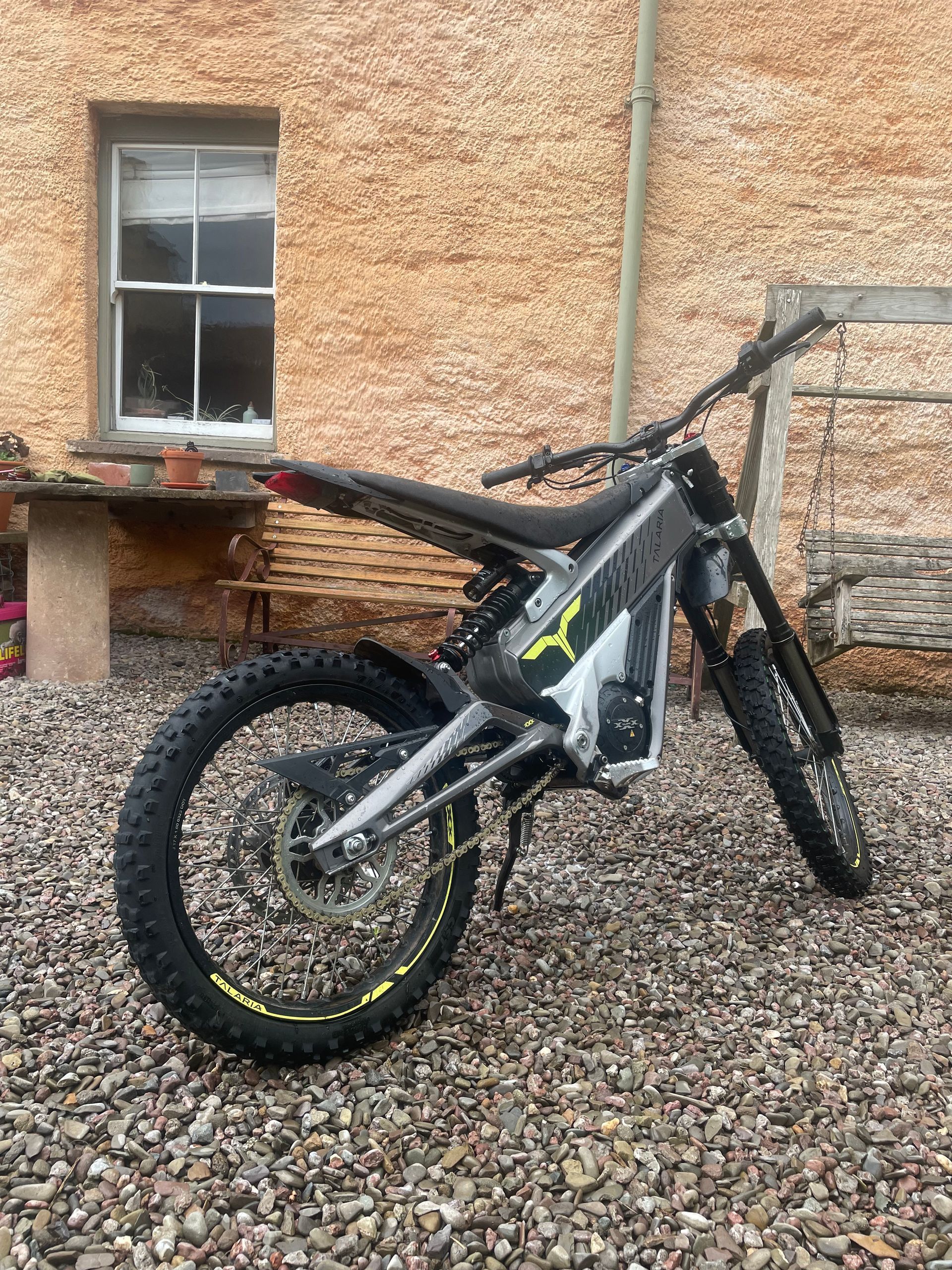 Electric dirt bike parked on gravel in front of a brick building.