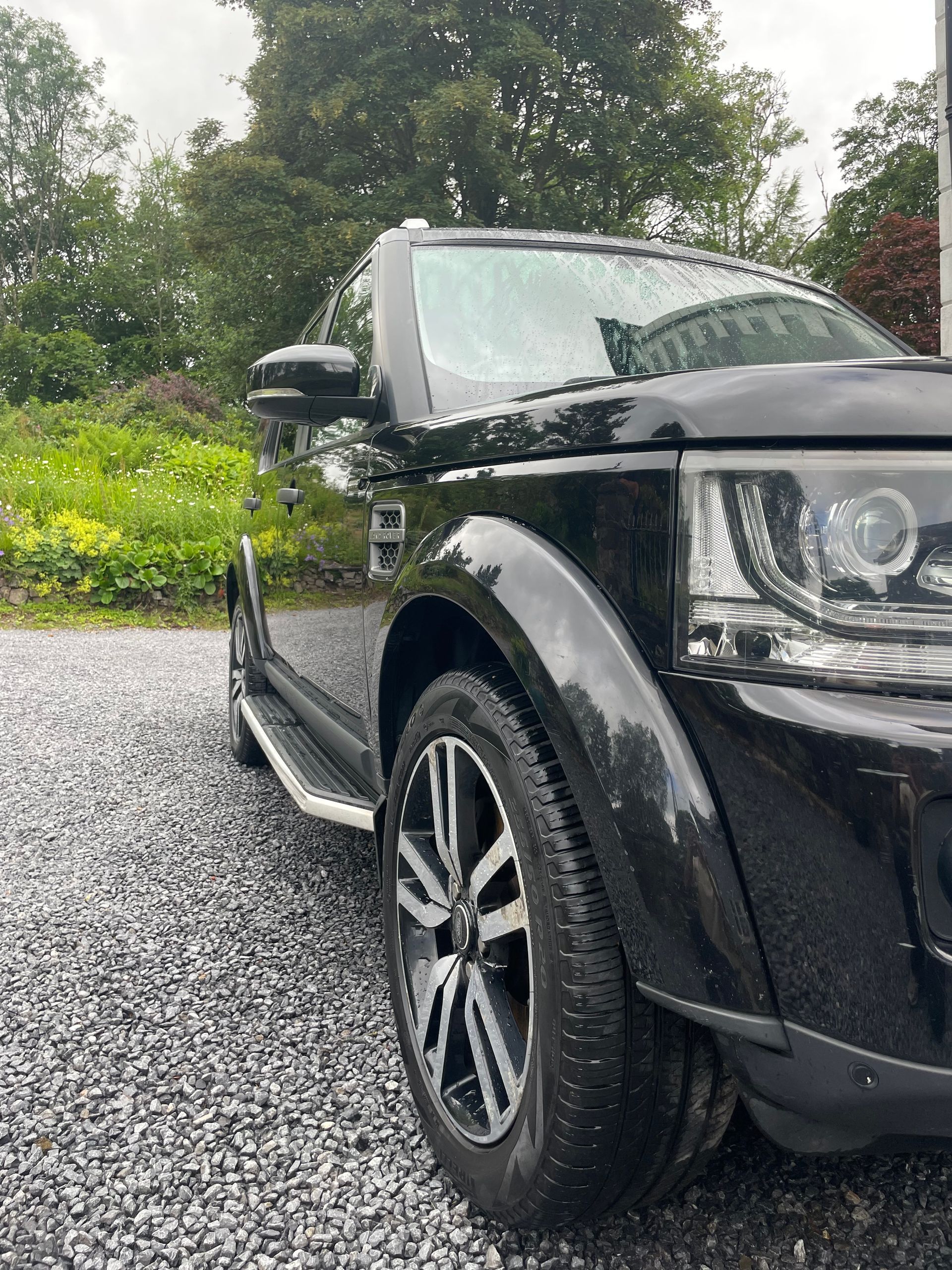 Black ceramic coated Land Rover Discovery SUV parked on gravel, wet from rain.