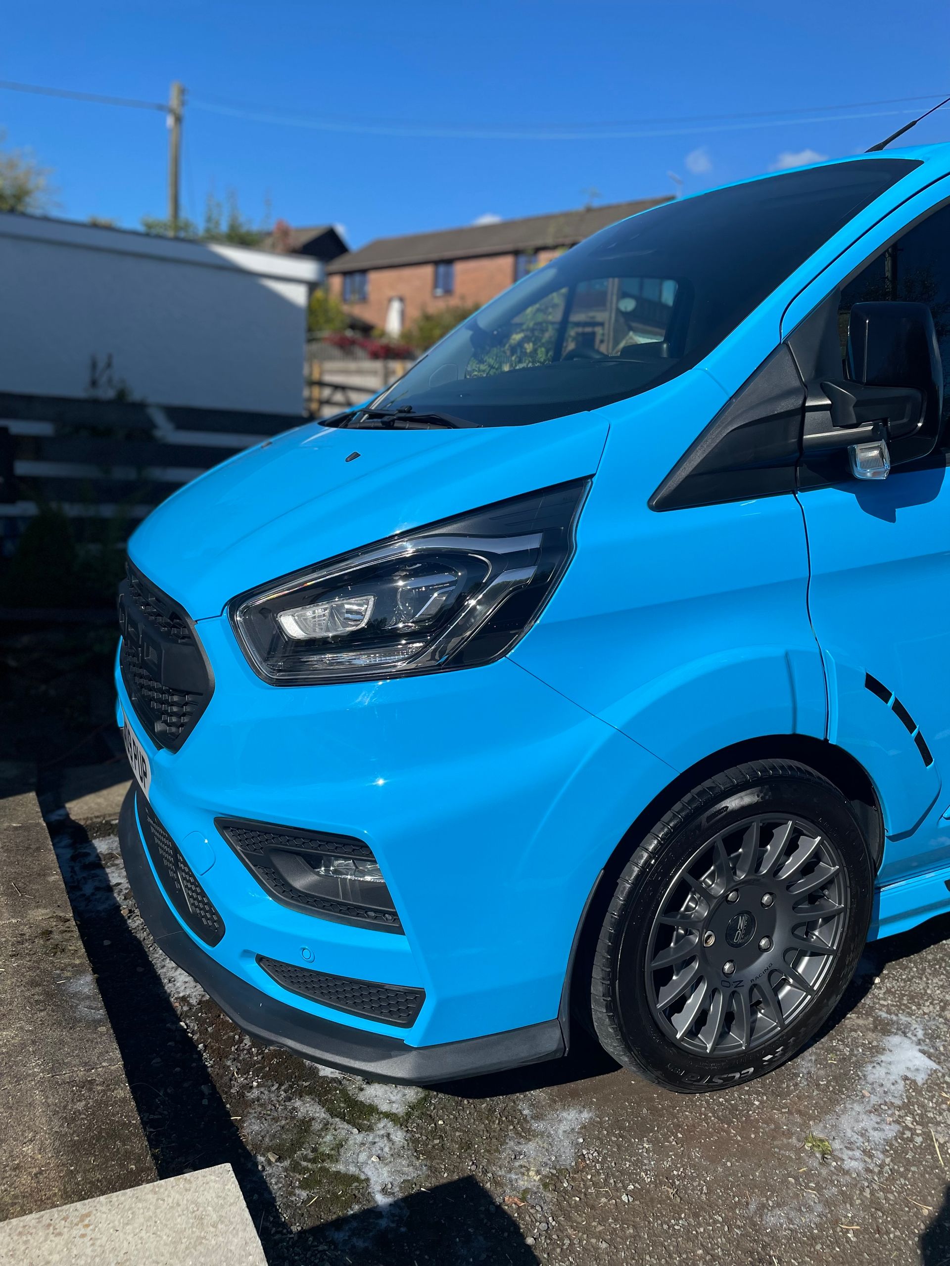 Bright blue custom van parked outdoors, dark wheels and black accents, under a clear sky.