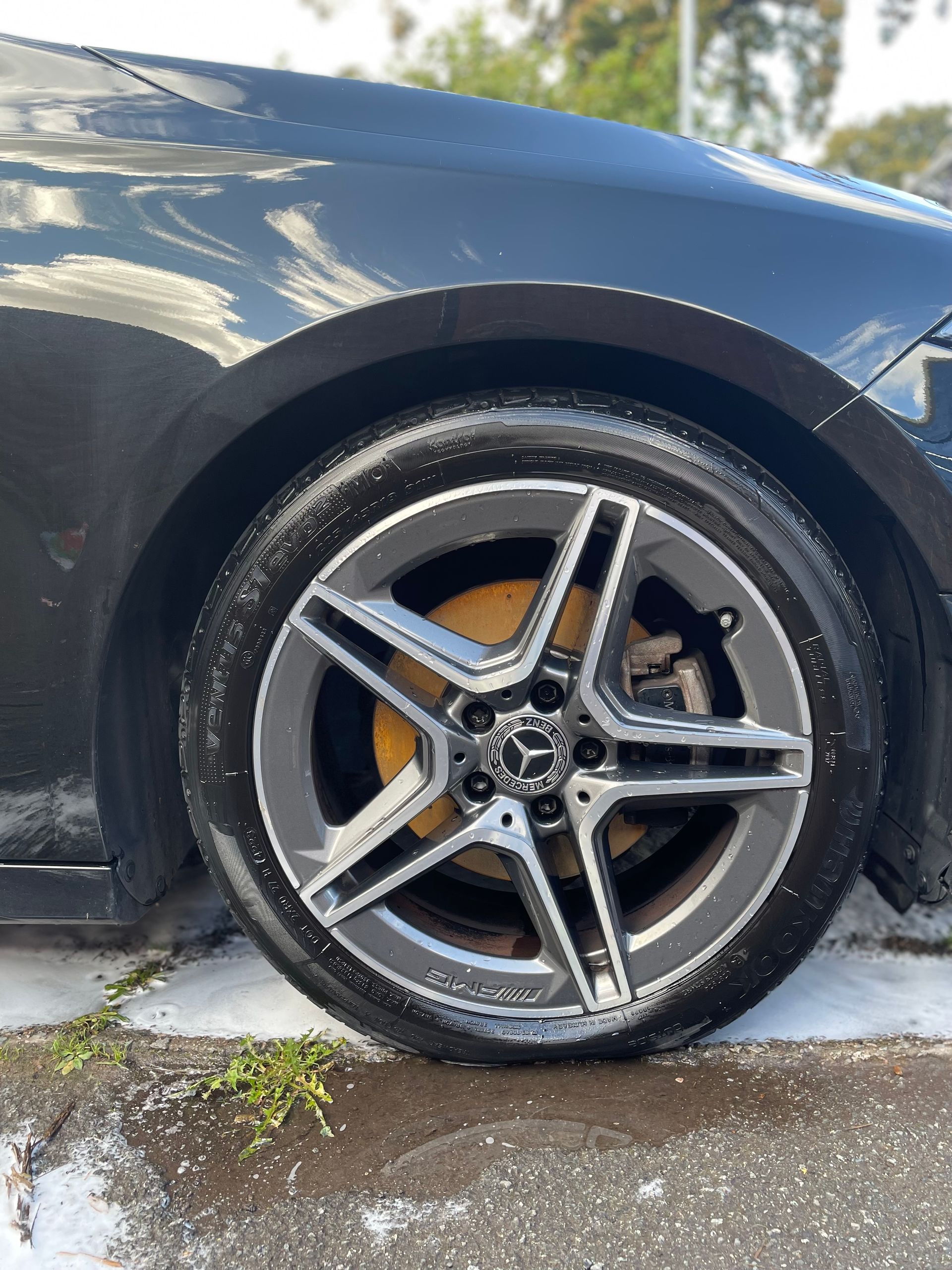 Black car wheel with a grey and silver rim, yellow brake caliper, and tyre shine applied to tyre.