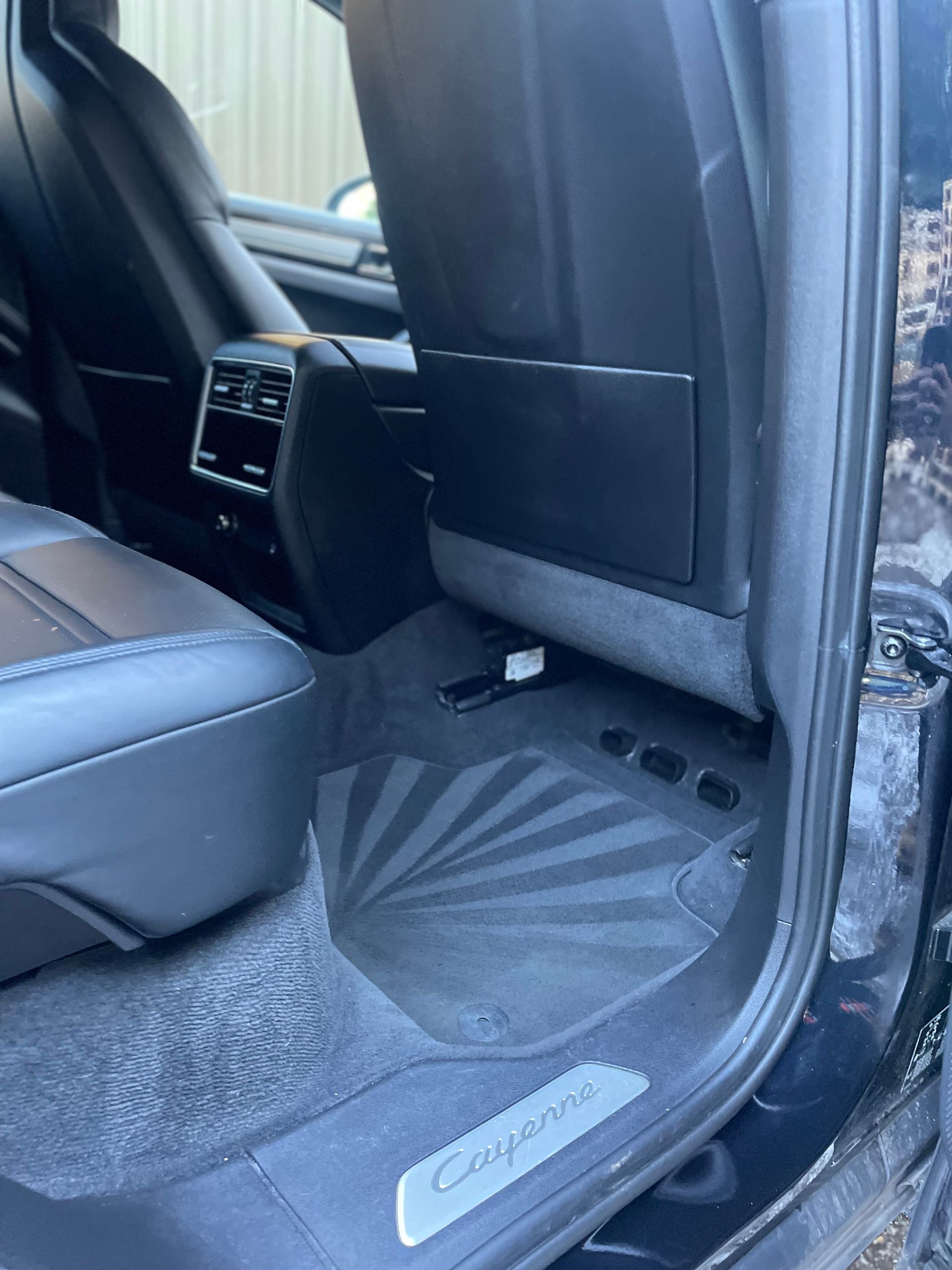 Interior view of a black car's rear seat, black leather, floor mats, and the door sill with “Cayenne” branding.