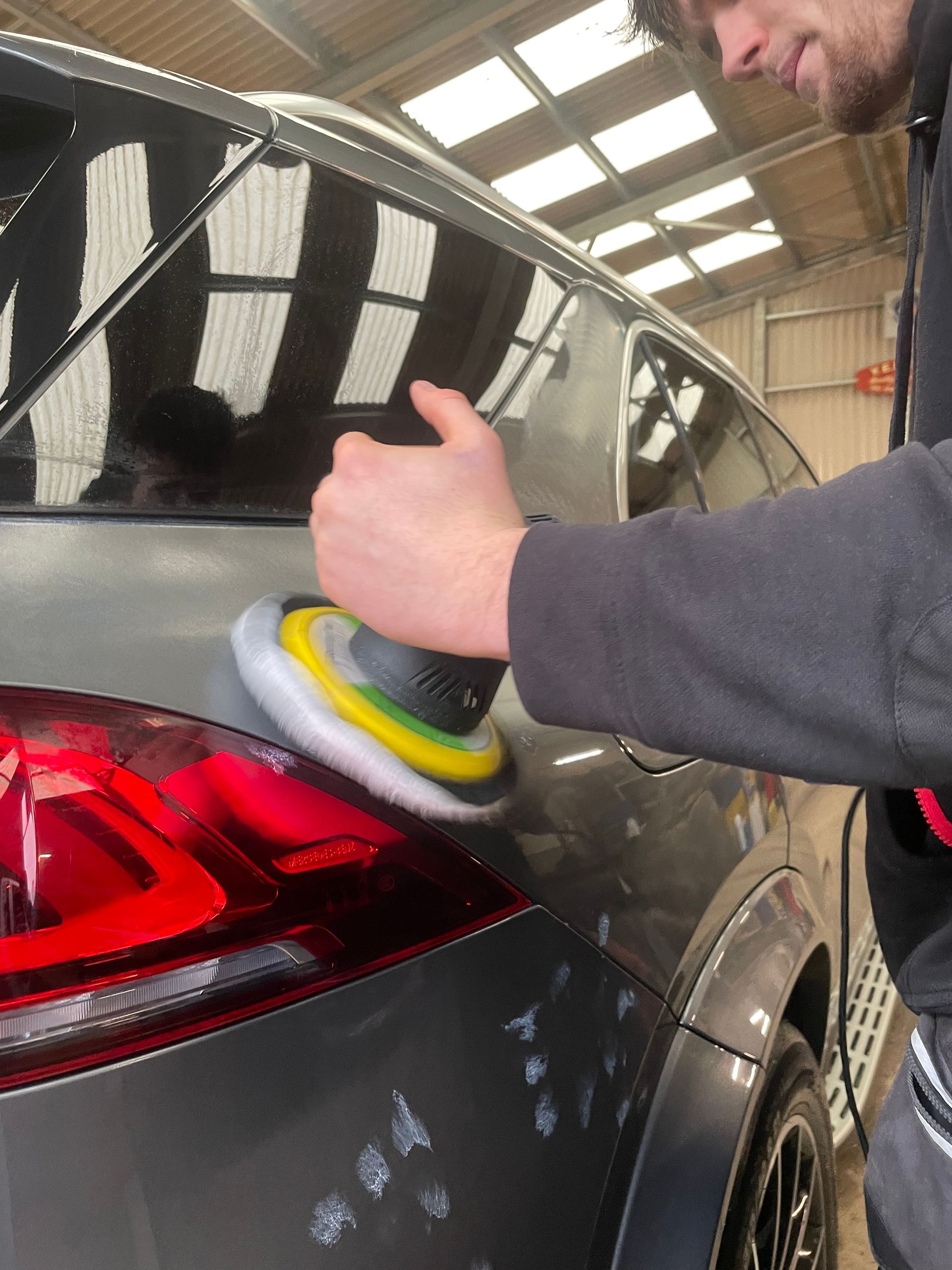 Accredited detailer polishing a grey car with a machine polisher.