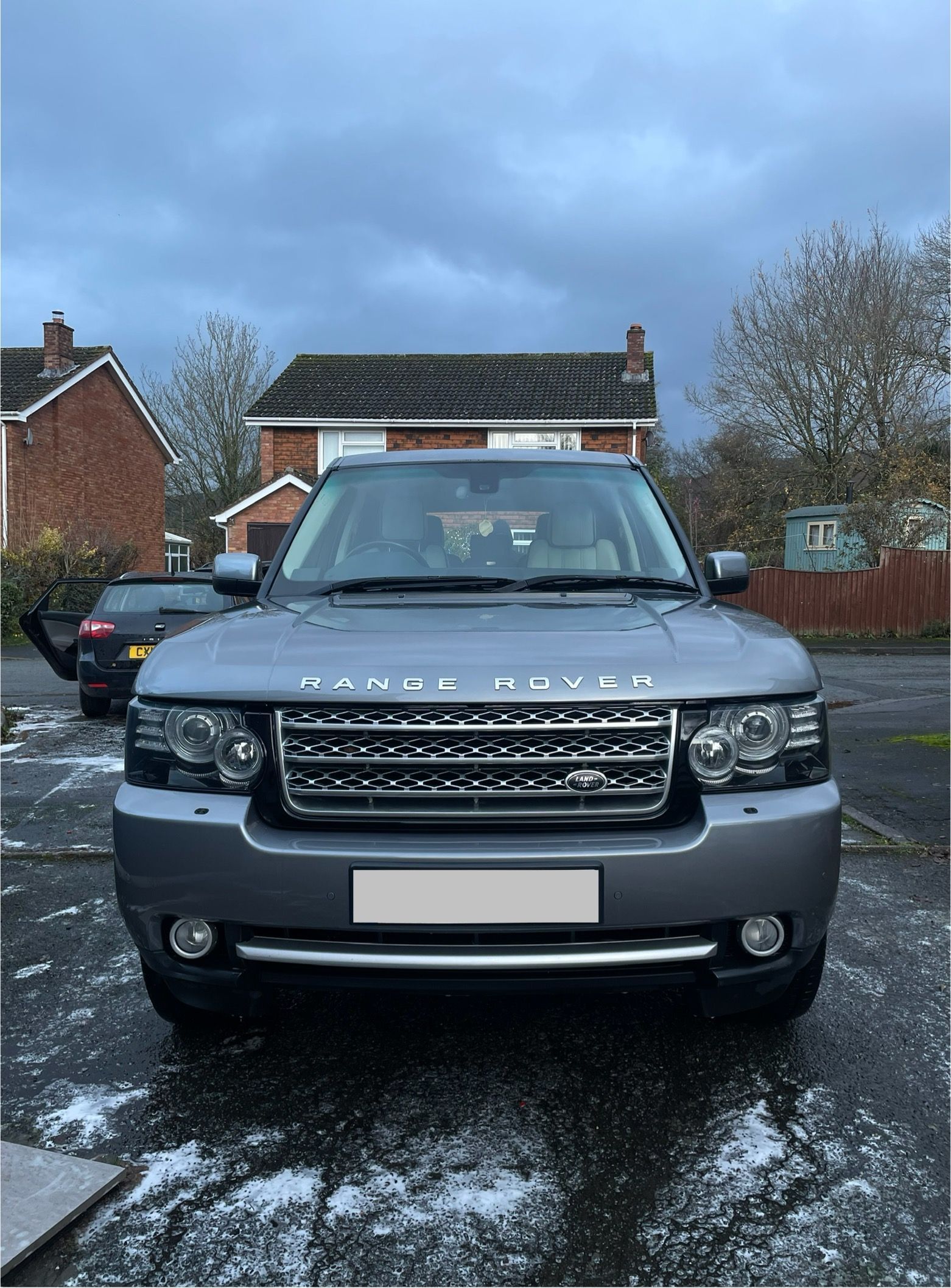 Silver Range Rover SUV parked on a driveway in front of a house on a cloudy day.