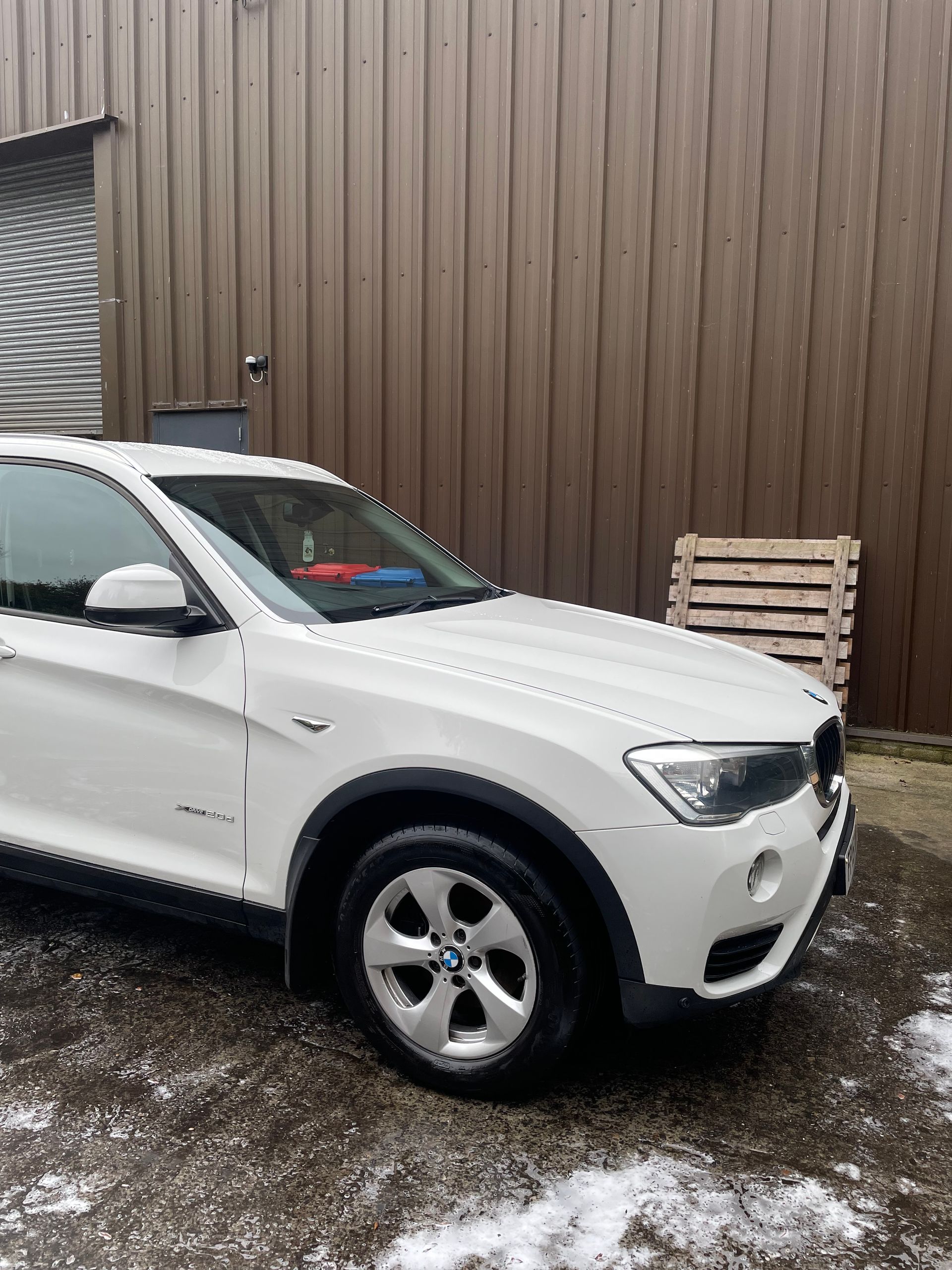 White BMW SUV parked outside a building with brown siding.