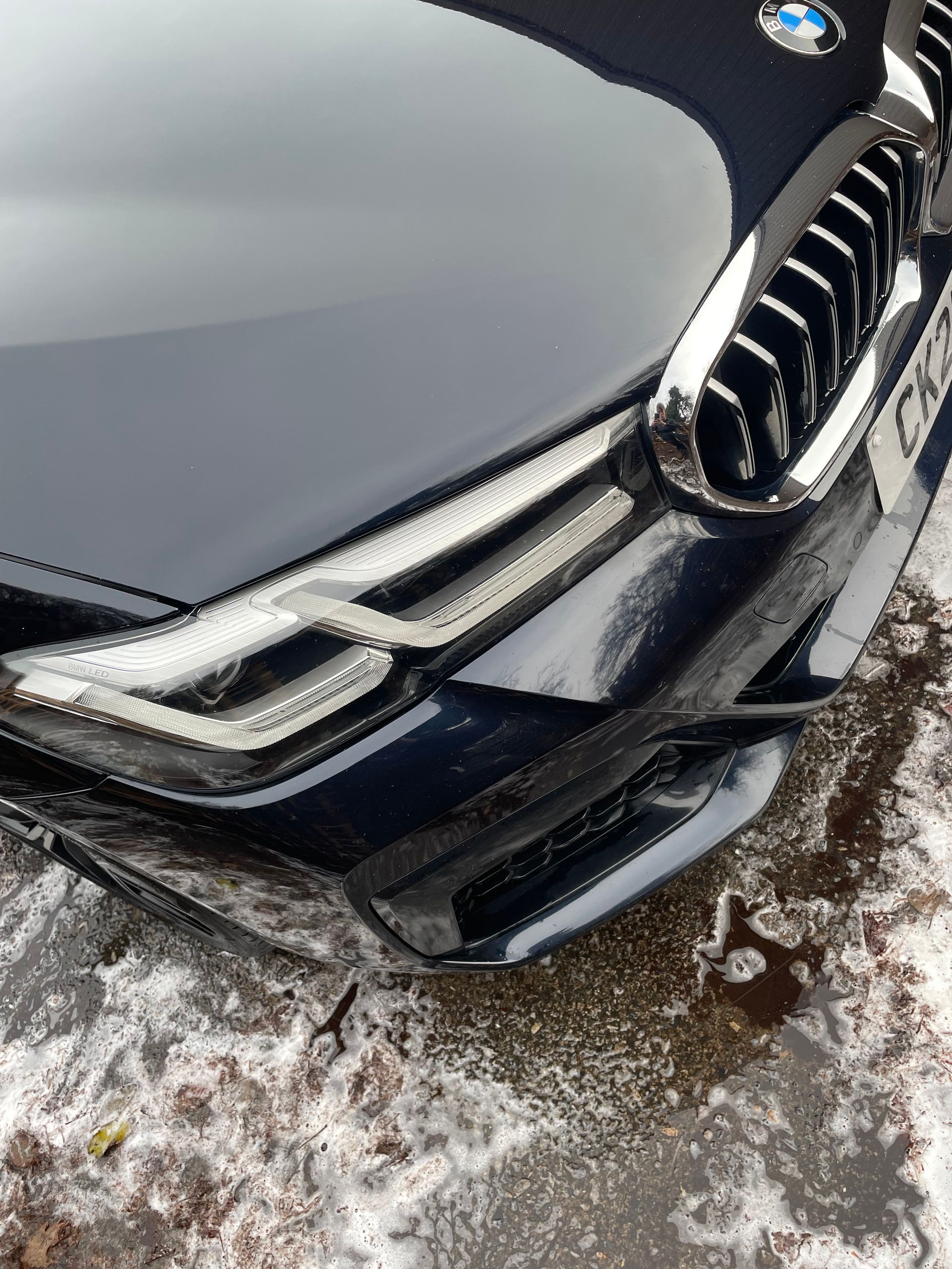 Black BMW car front with chrome detailing, parked on a snowy surface.