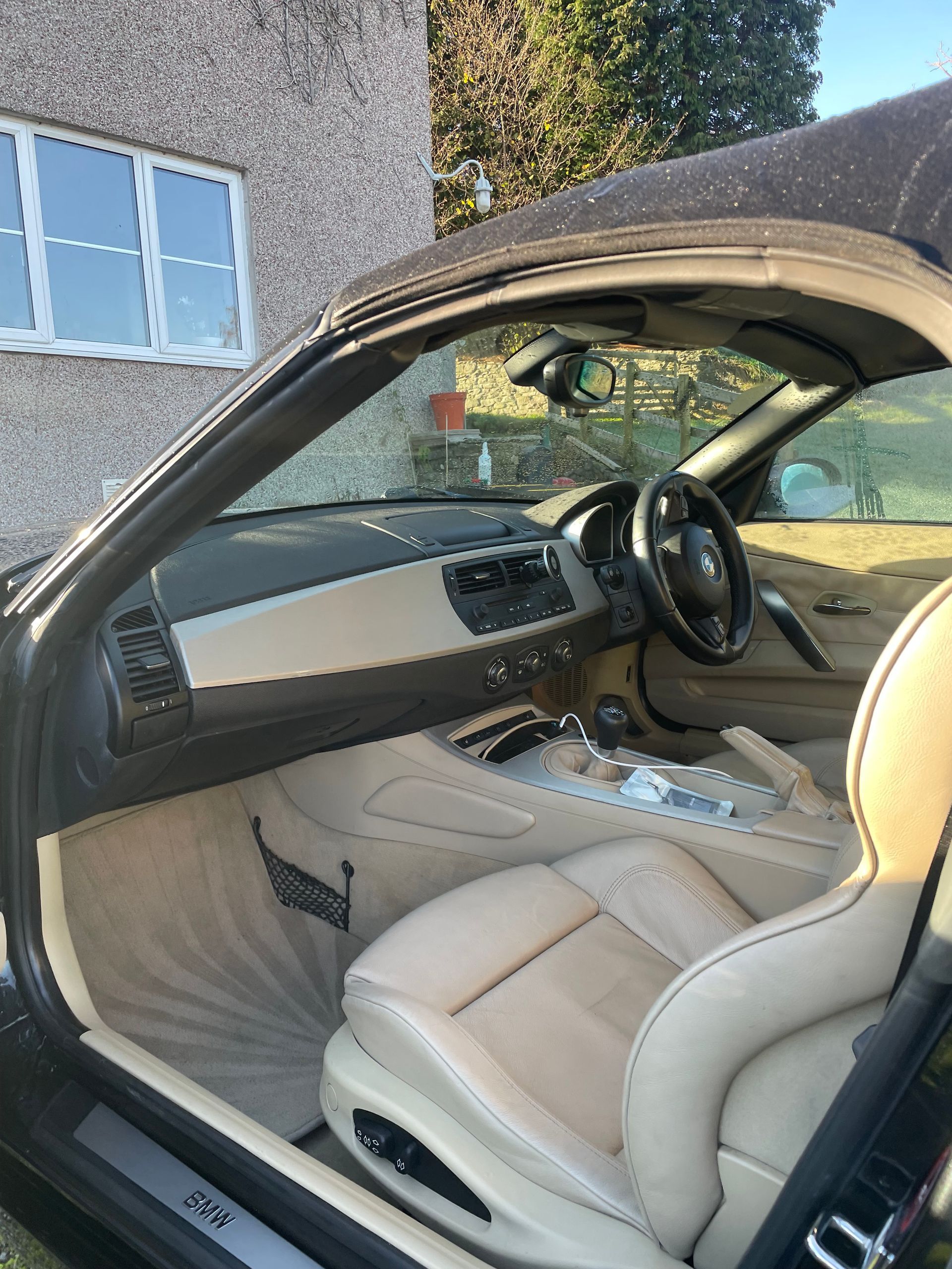 Interior of a black BMW Z4 convertible. Beige leather seats and dashboard, steering wheel visible.