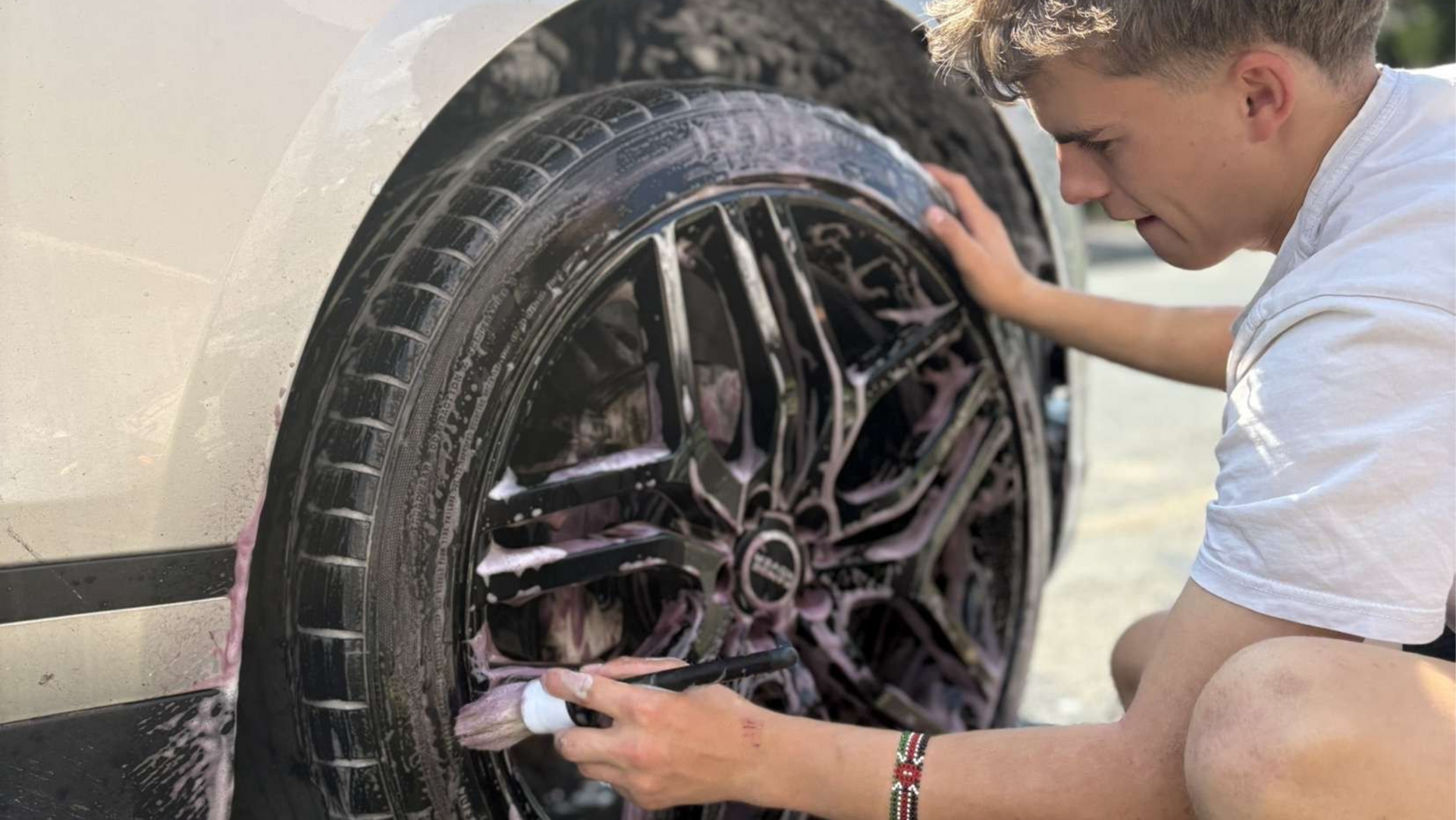 A detailer deep cleaning and decontaminating a black Range Rover wheel ready for ceramic coating