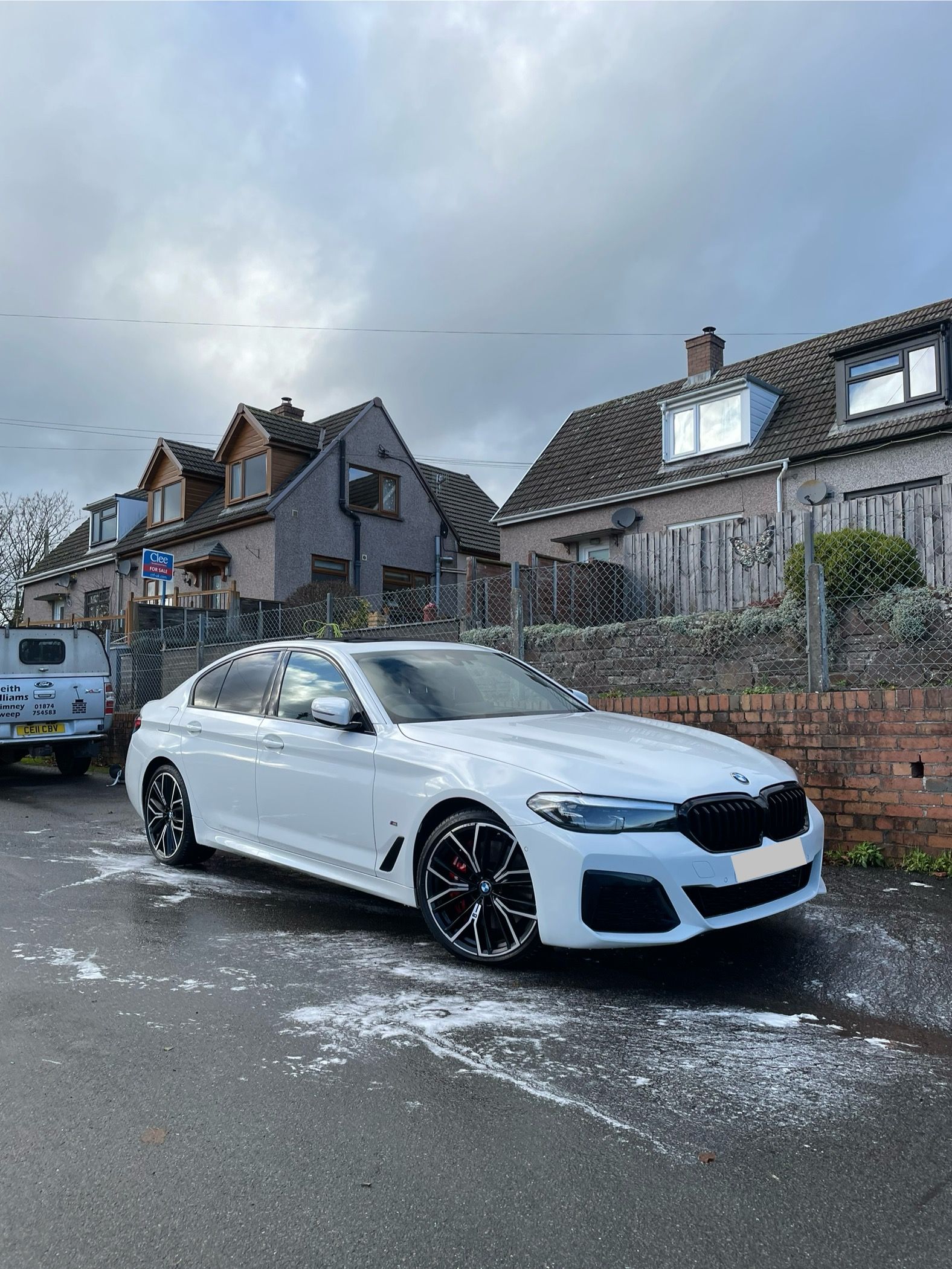 White BMW sedan parked on a street with houses in the background. Cloudy sky.