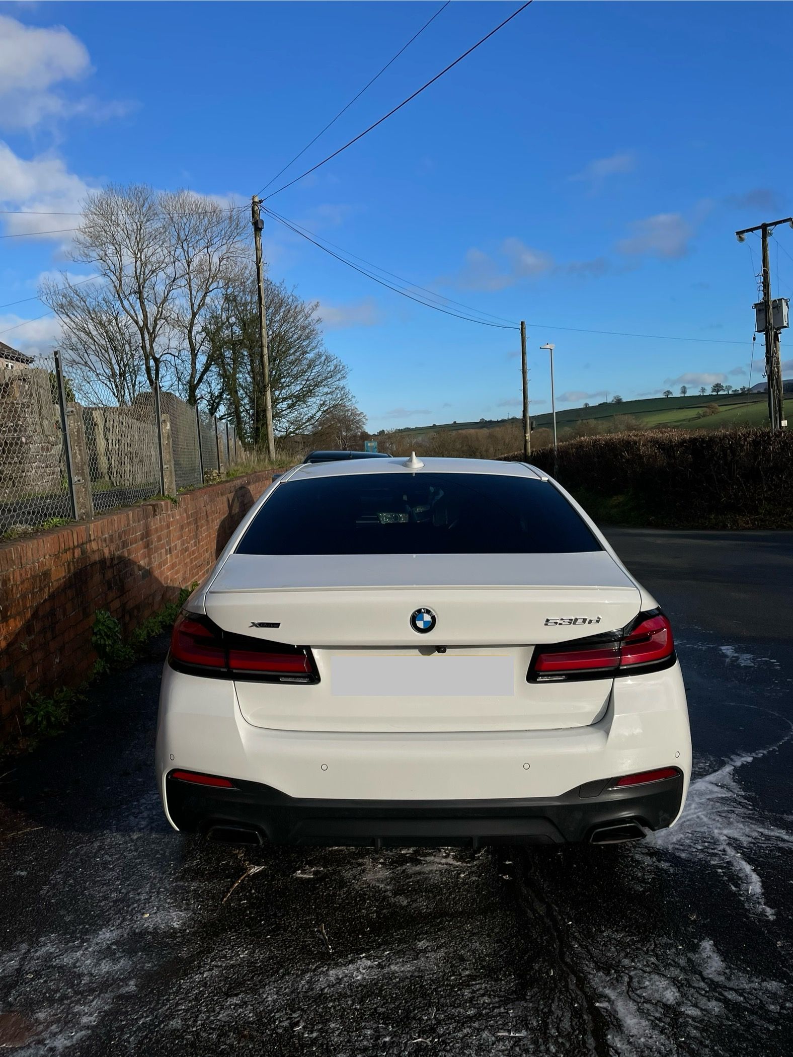 White BMW sedan parked on a wet road, sunny day.