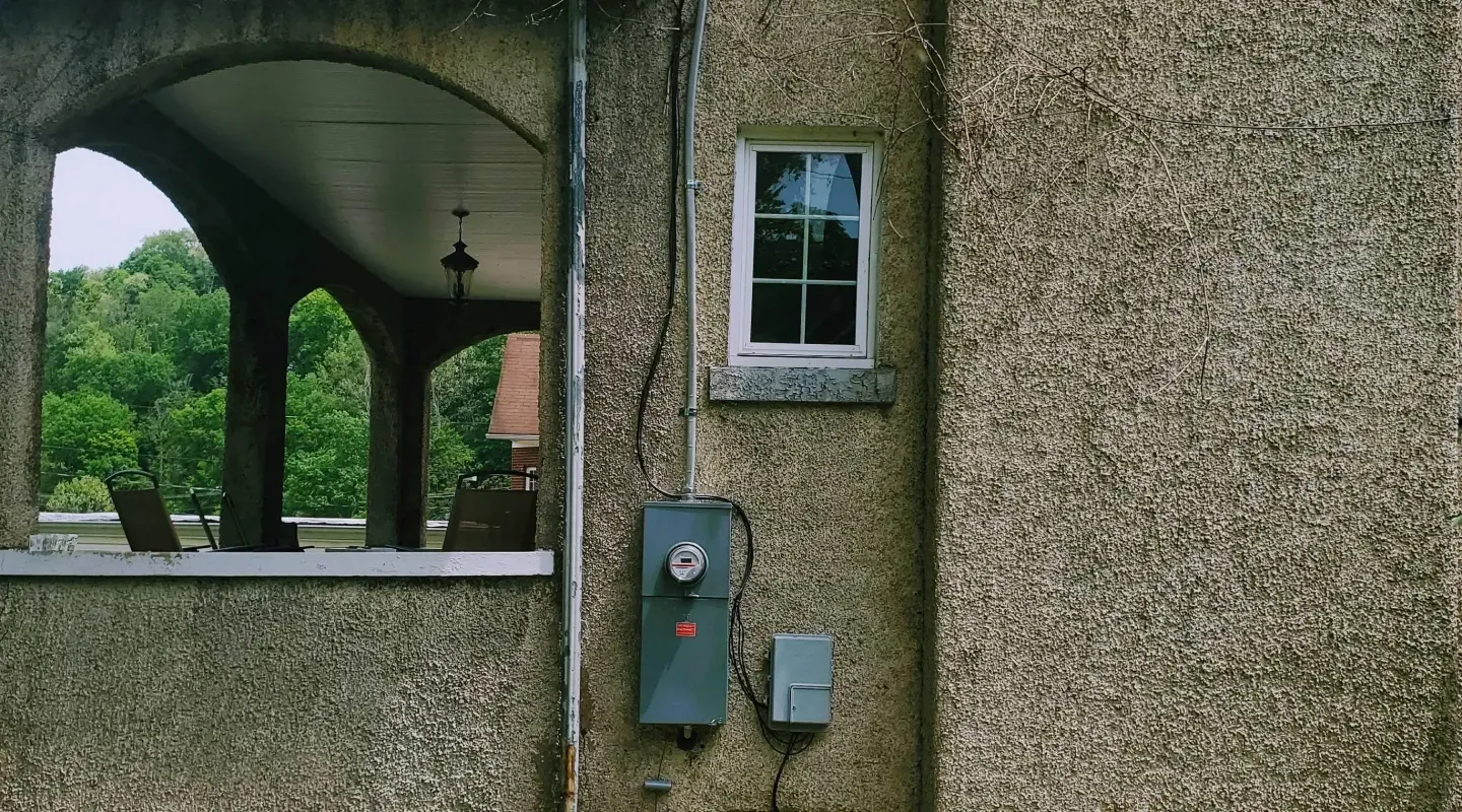 Exterior wall with textured brown finish, an arched porch entrance, a small window, and mounted electrical equipment.