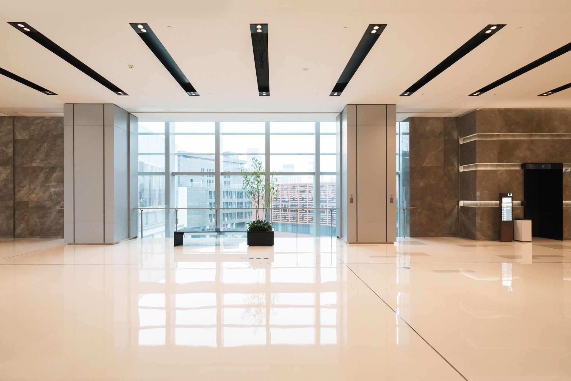 A bright, minimalist office lobby with white marble floors, large windows, recessed ceiling lights, and stone columns.