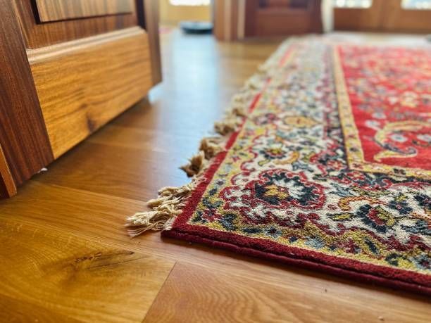 Close-up of a decorative rug with red, white, and gold patterns resting on light-colored wooden flooring.