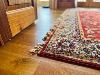 Close-up of a decorative rug with red, white, and gold patterns resting on light-colored wooden flooring.