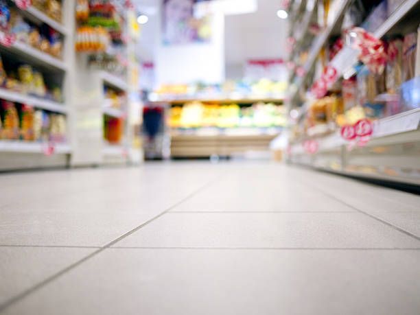 Low-angle view of a grocery store aisle with white tile flooring between rows of blurred shelves.