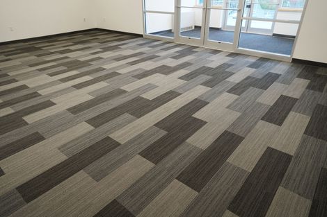 Interior view of a modern room with gray-toned, rectangular carpet tiles arranged in a staggered, linear pattern.