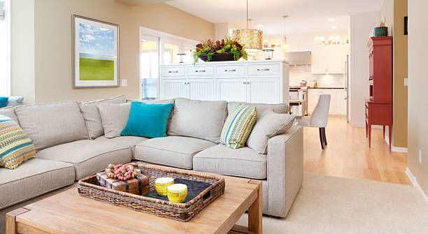 A beige sectional sofa with teal and striped pillows sits in a living room with a wooden coffee table and white cabinetry.