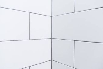 White rectangular subway tiles on two walls meeting at a corner with dark grout lines.