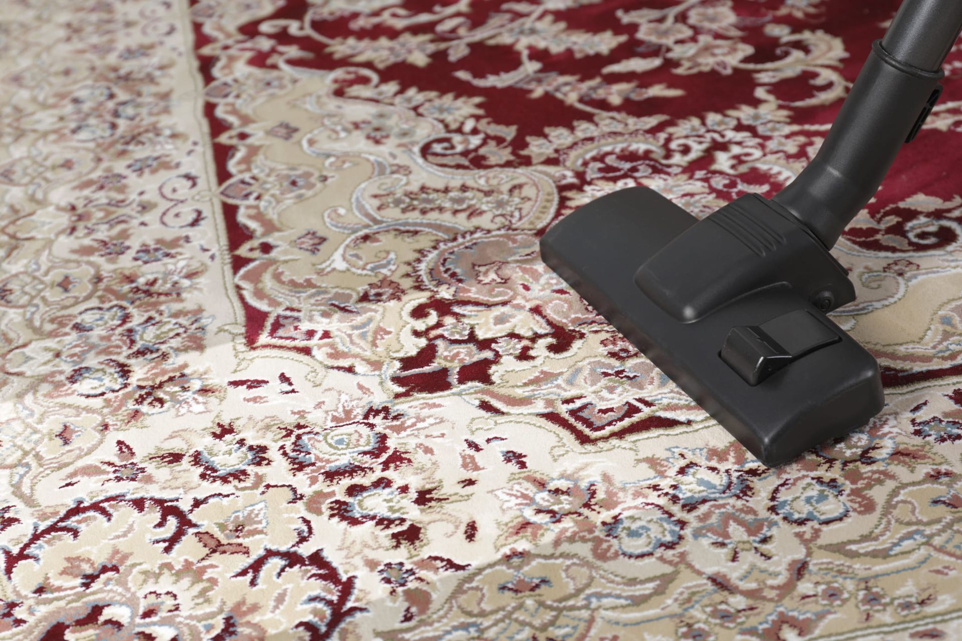 A vacuum cleaner nozzle cleaning a section of a patterned red and beige oriental-style area rug.