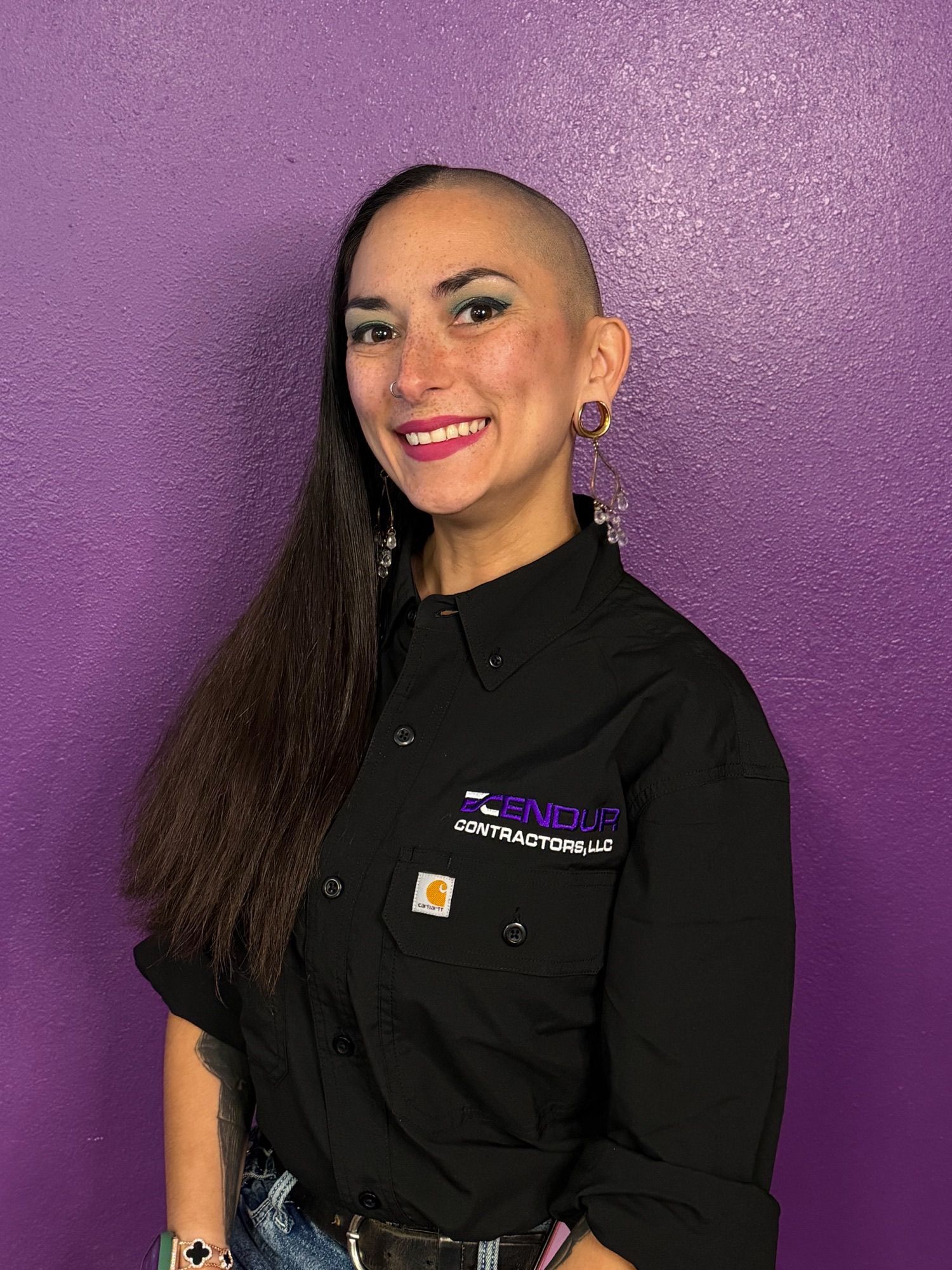 Person in a black shirt smiling against a purple wall.