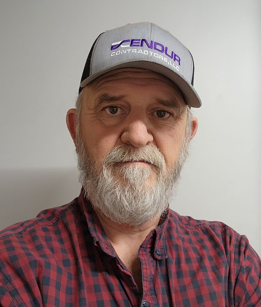Man wearing a trucker hat and plaid shirt, looking directly at the viewer.