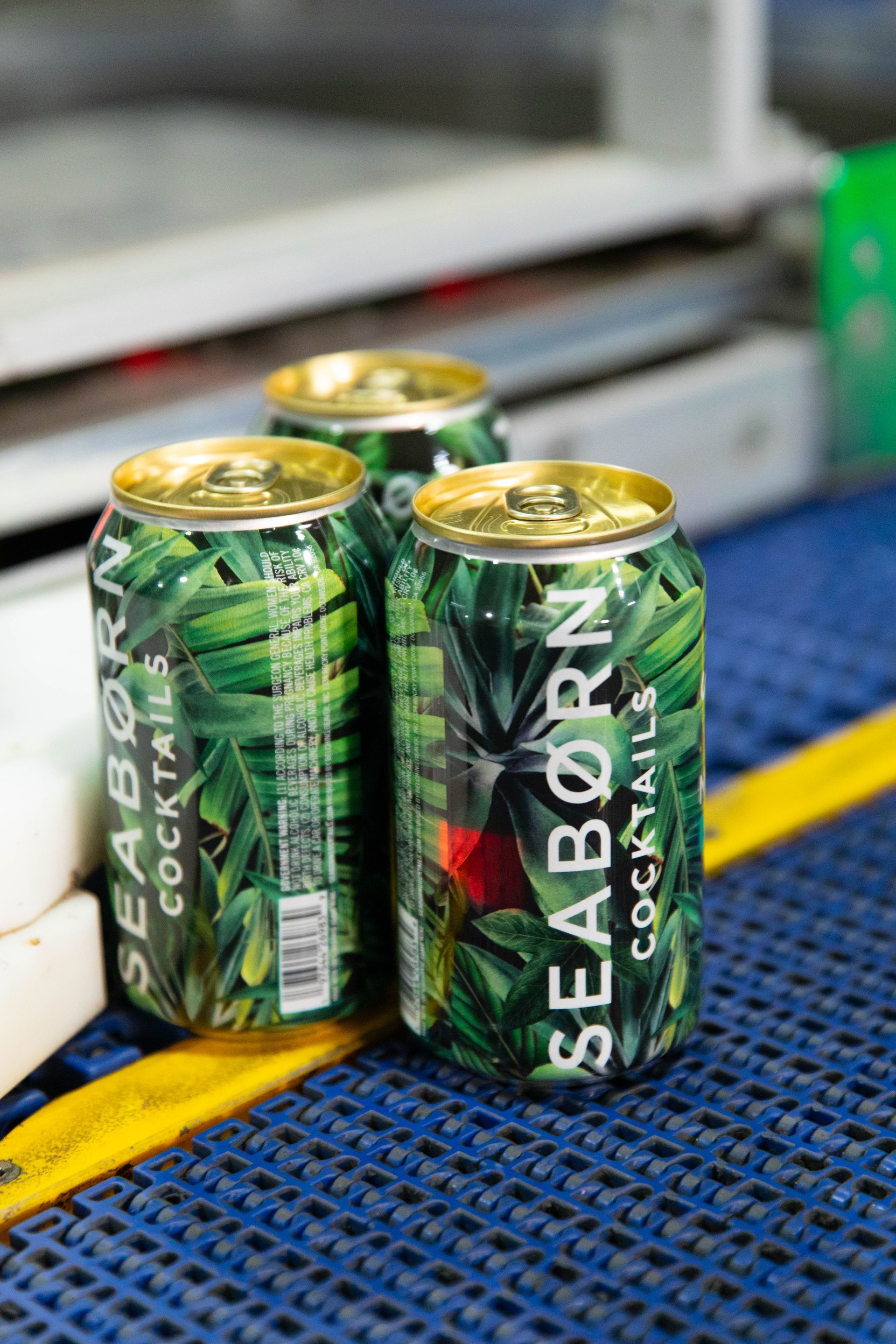 three cans of seaborn cocktails are sitting on a conveyor belt .