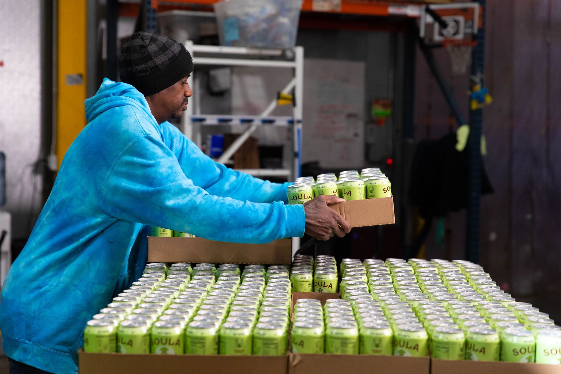 a man in a blue hoodie is holding a box of cans .