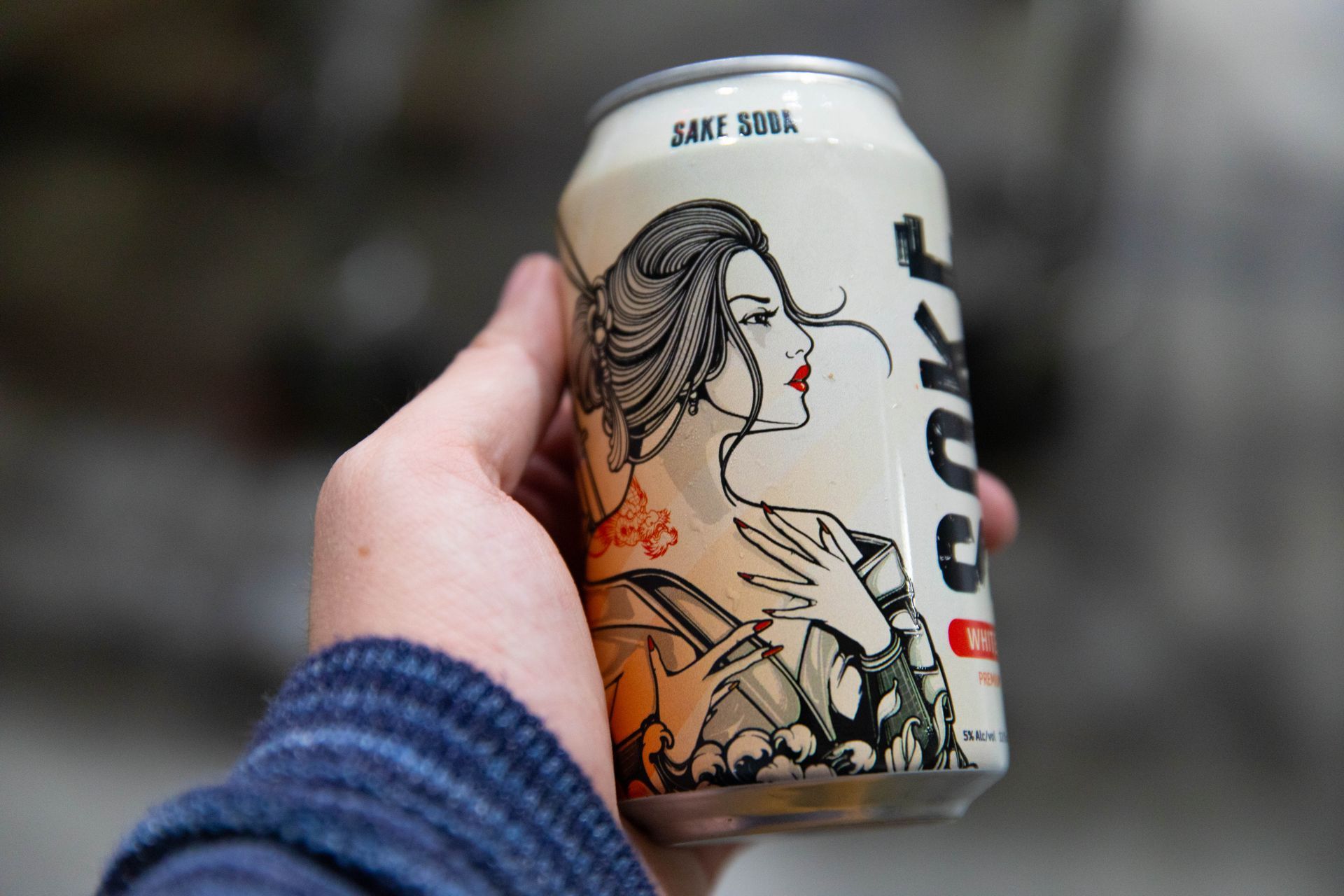 a person is holding a can of beer with a geisha on it .