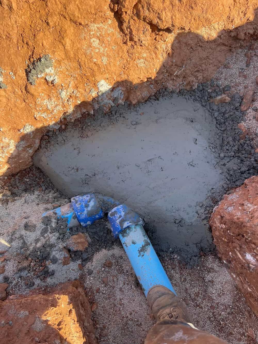 Blue PVC Pipes and Fittings Embedded in Wet Cement Within a Dirt Trench — D & B Plumbing NQ in Trinity Beach, QLD