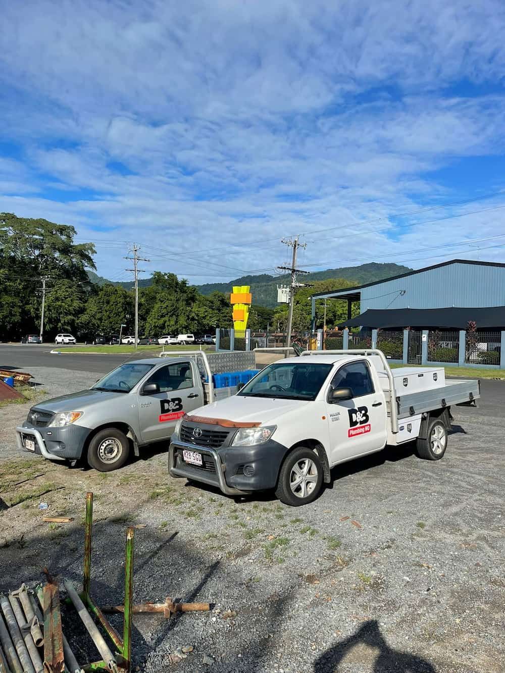 Two Work Trucks Parked on Gravel in Front of a Building — D & B Plumbing NQ in Kanimbla, QLD