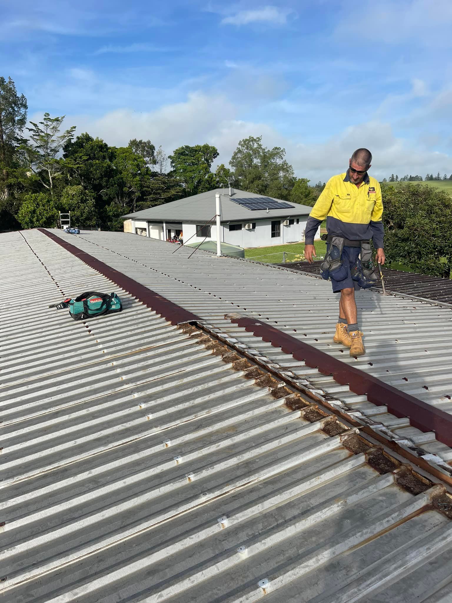 Person in Yellow Shirt on a Corrugated Metal Roof — D & B Plumbing NQ in Trinity Beach, QLD