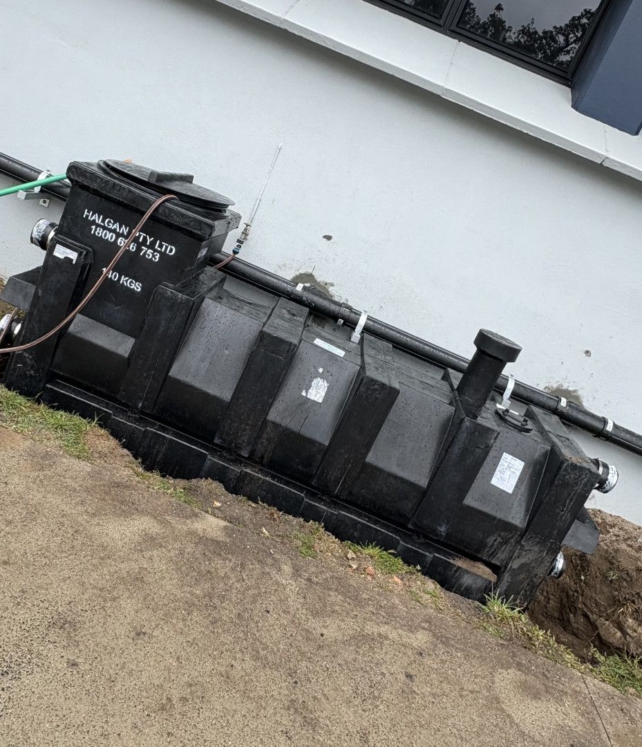 Black rectangular septic tank outside a building, partially buried in a trench.