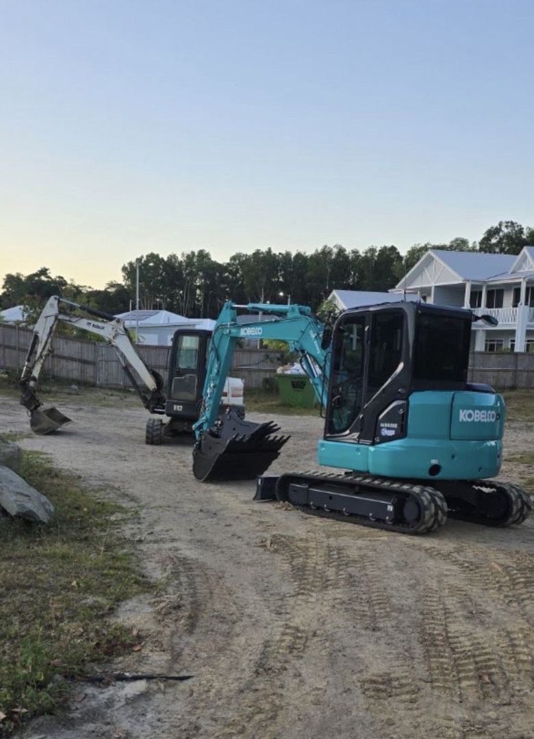 Two teal and black excavators on a dirt surface.