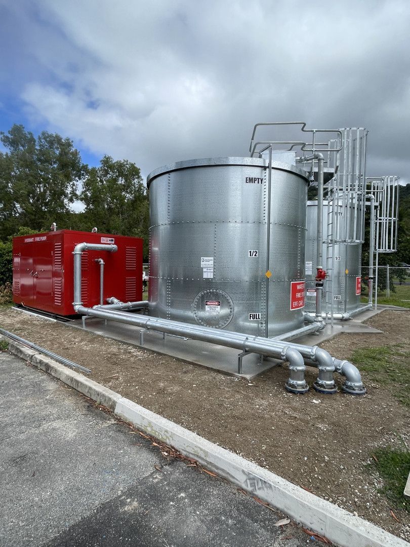 Silver industrial tanks and red equipment against a cloudy sky.