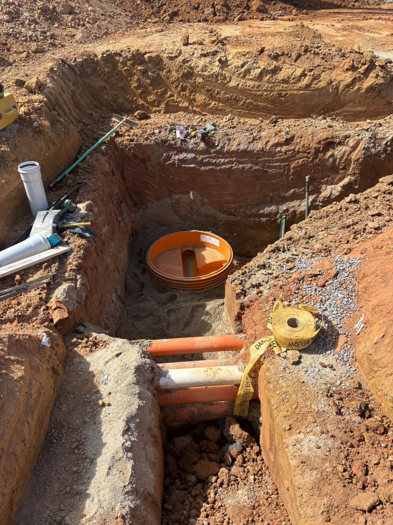 Excavated ground reveals a buried orange septic tank and pipes during a construction project.