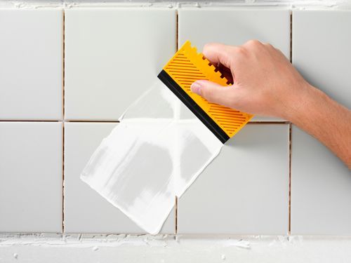 A person is cleaning a tile wall with a spatula.