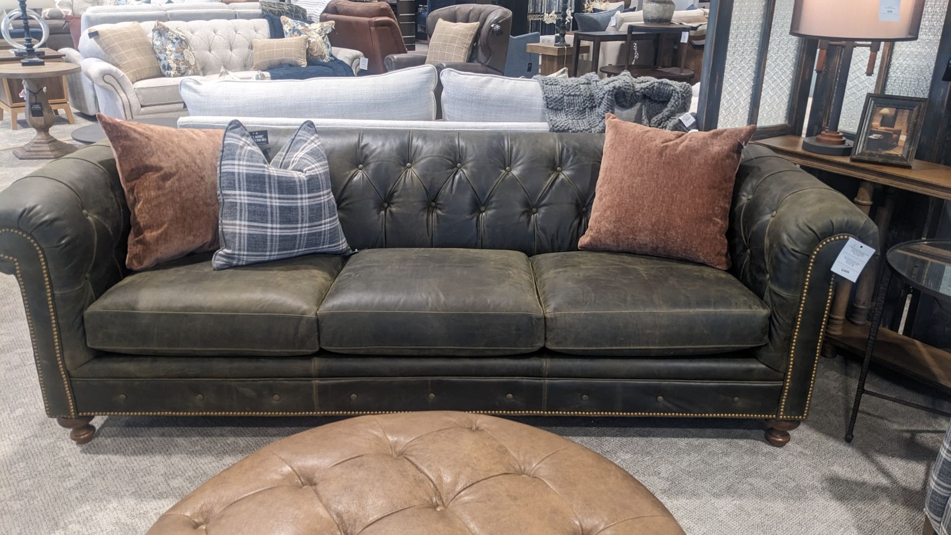A leather couch with pillows and an ottoman in a living room.