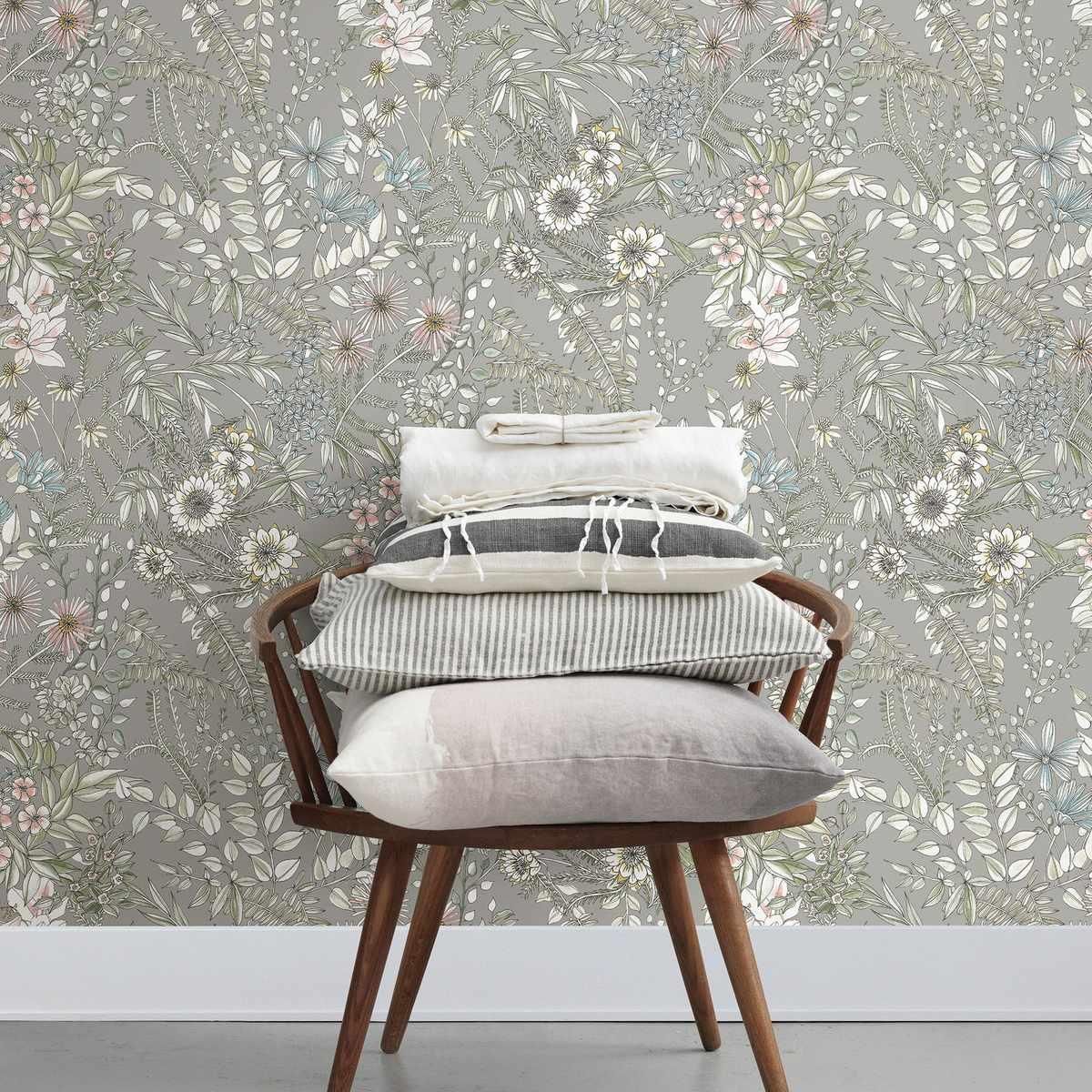 A chair with a stack of pillows on it in front of a floral wallpaper.
