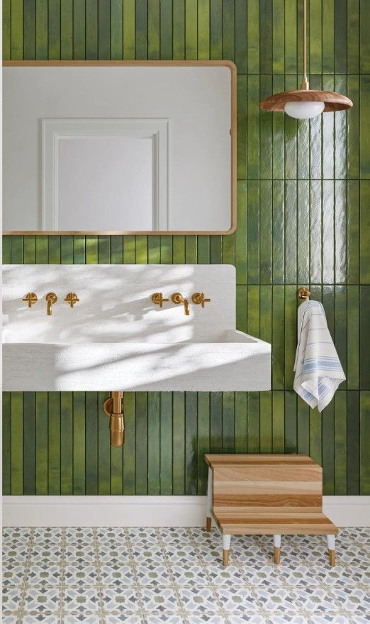 A bathroom with green tiles , a sink and a mirror.