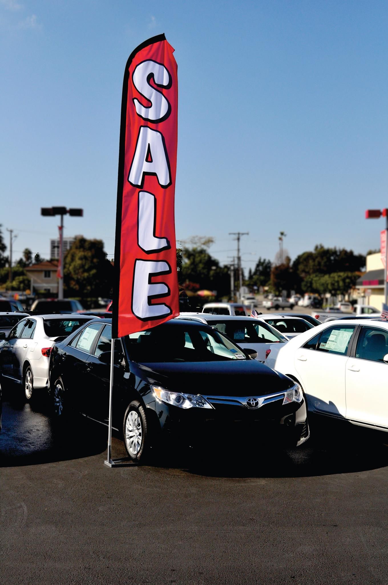 A black car is parked next to a red flag that says sale
