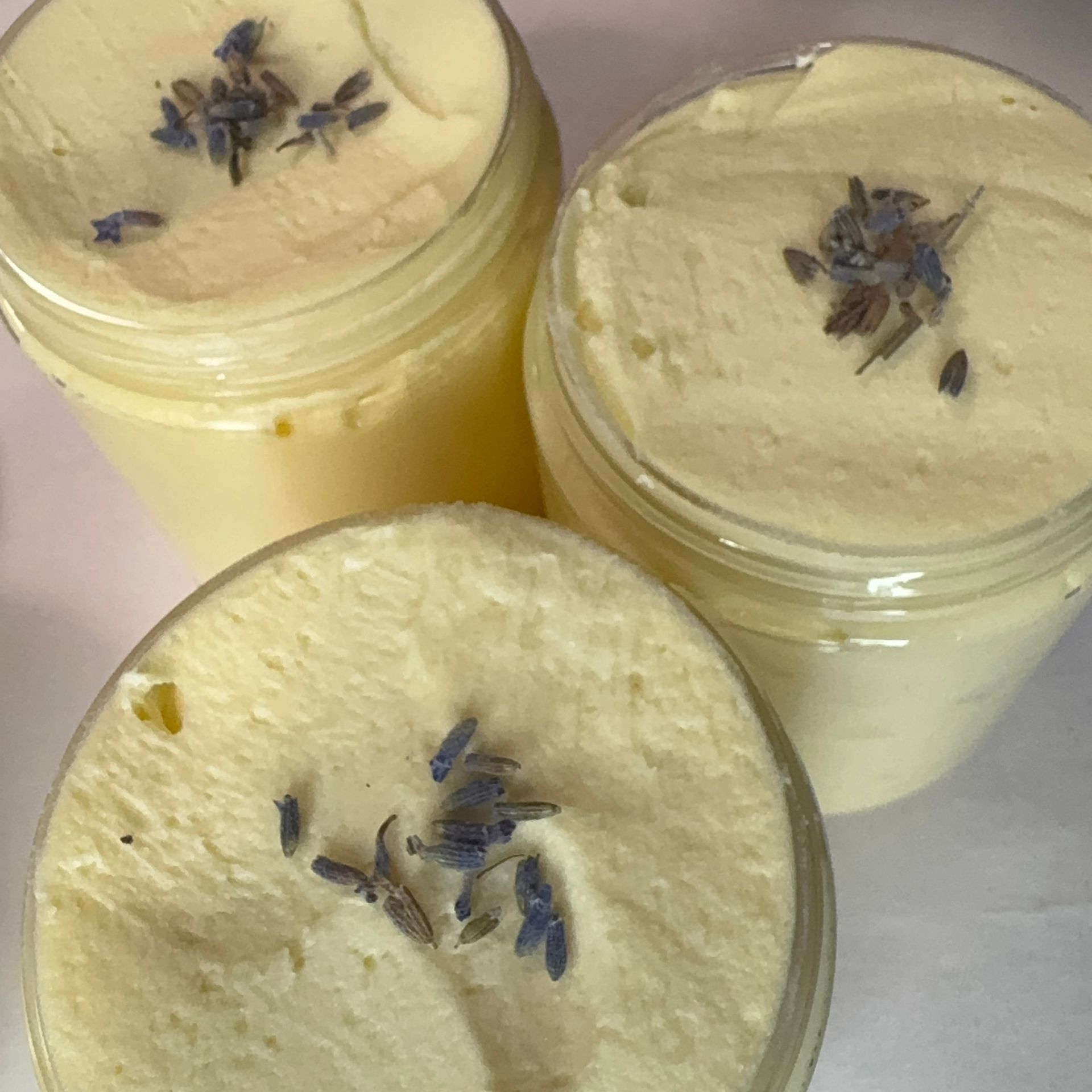 Jar of Kaimila Lazy Lavender body butter with green, purple, and white labels, set against a wood background.