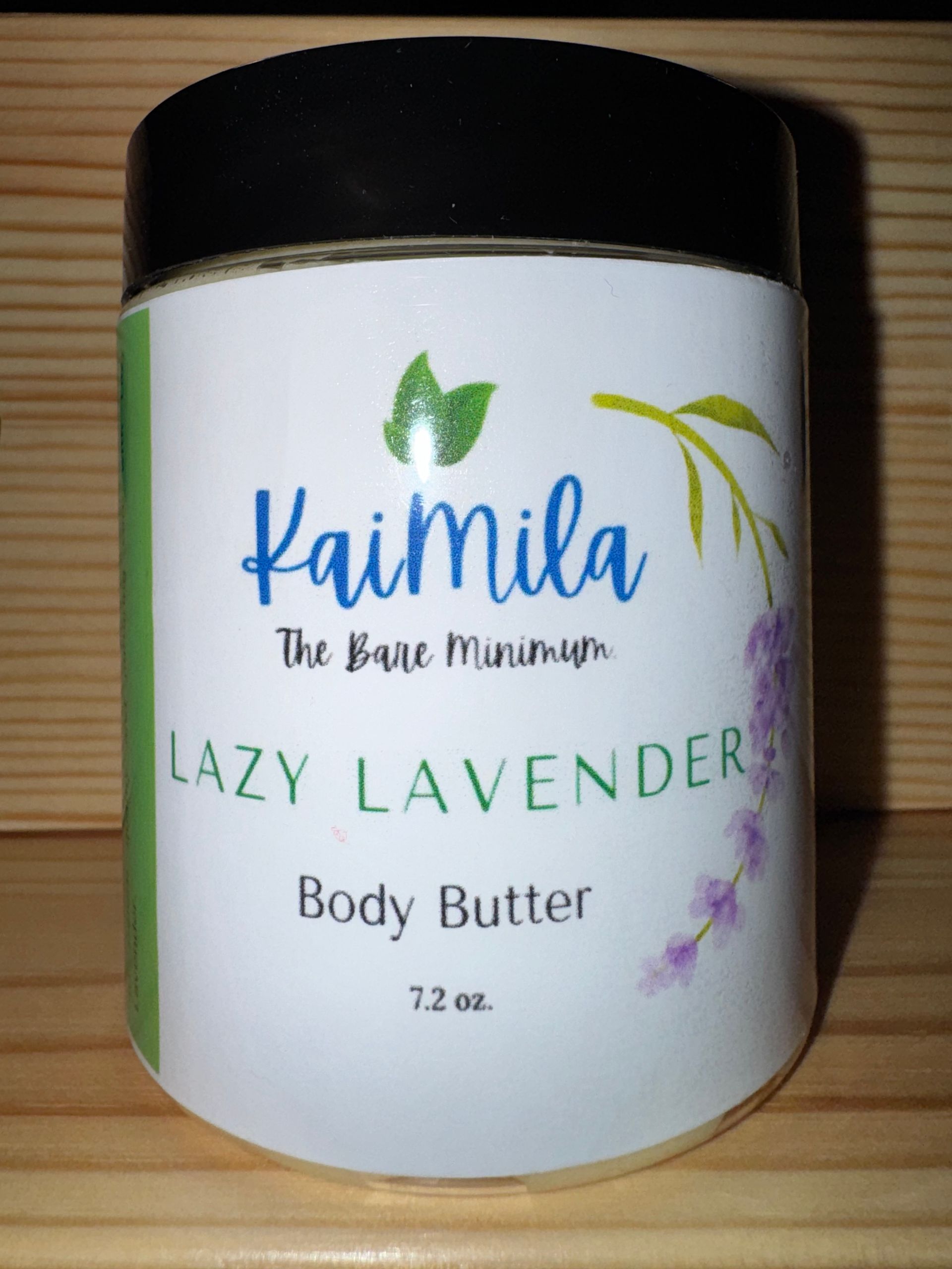 Jar of Kaimila Lazy Lavender body butter with green, purple, and white labels, set against a wood background.