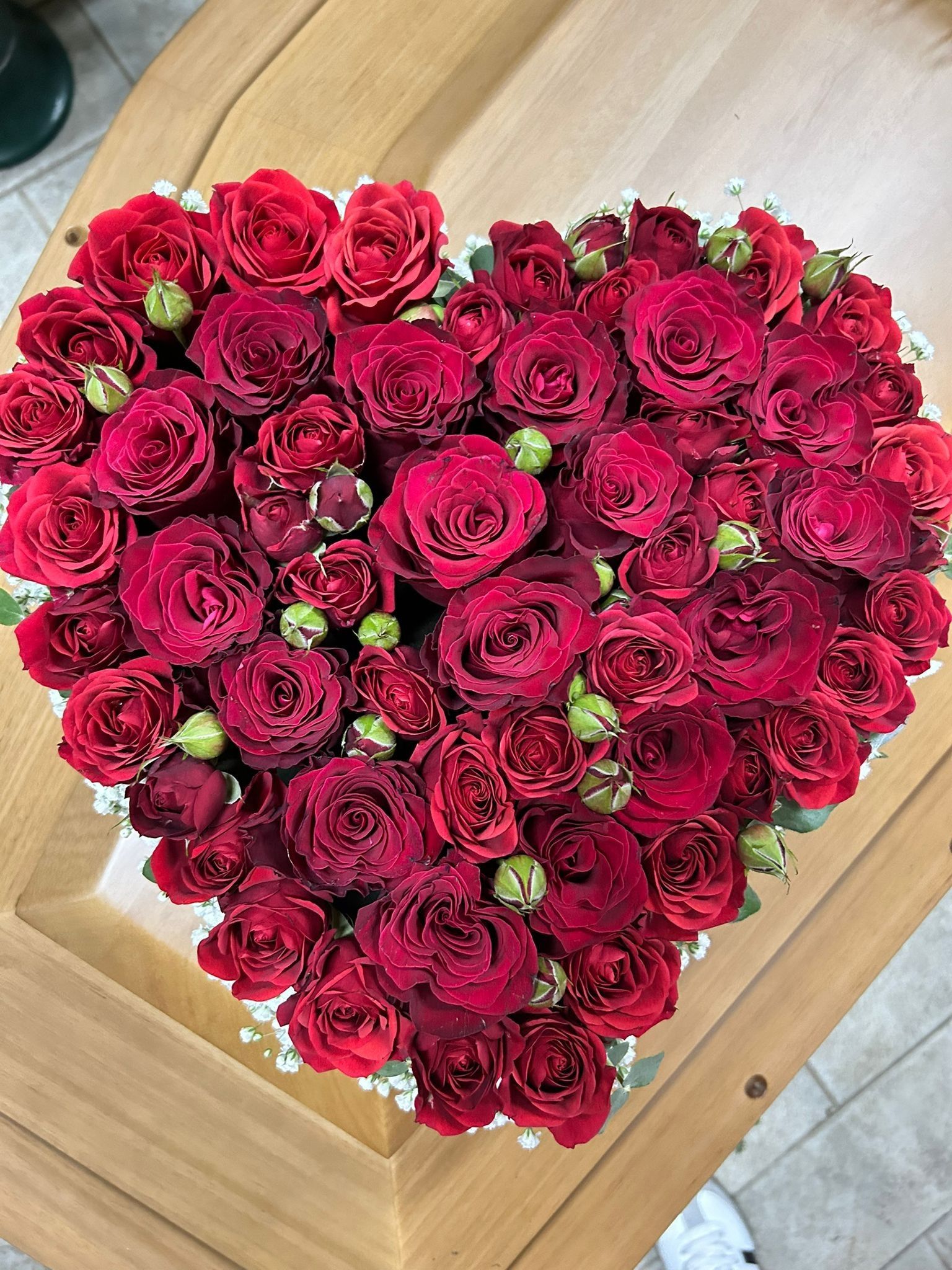 Composizione a forma di cuore di rose rosse e boccioli su una superficie di legno.