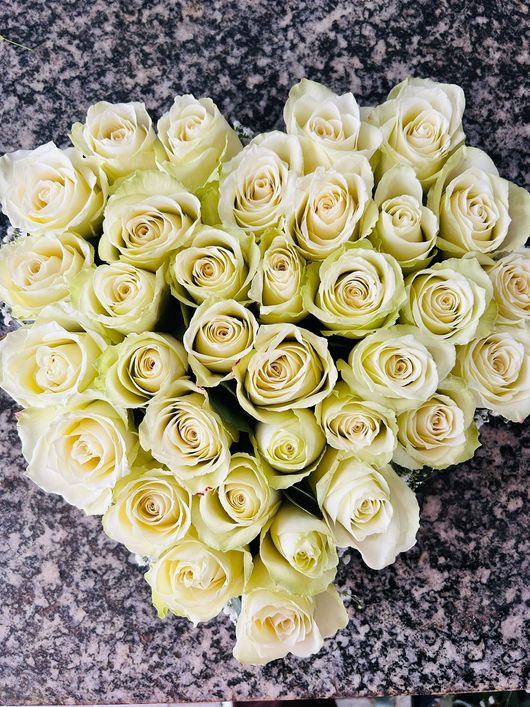 Rose bianche disposte a forma di cuore su una superficie grigia decorata.